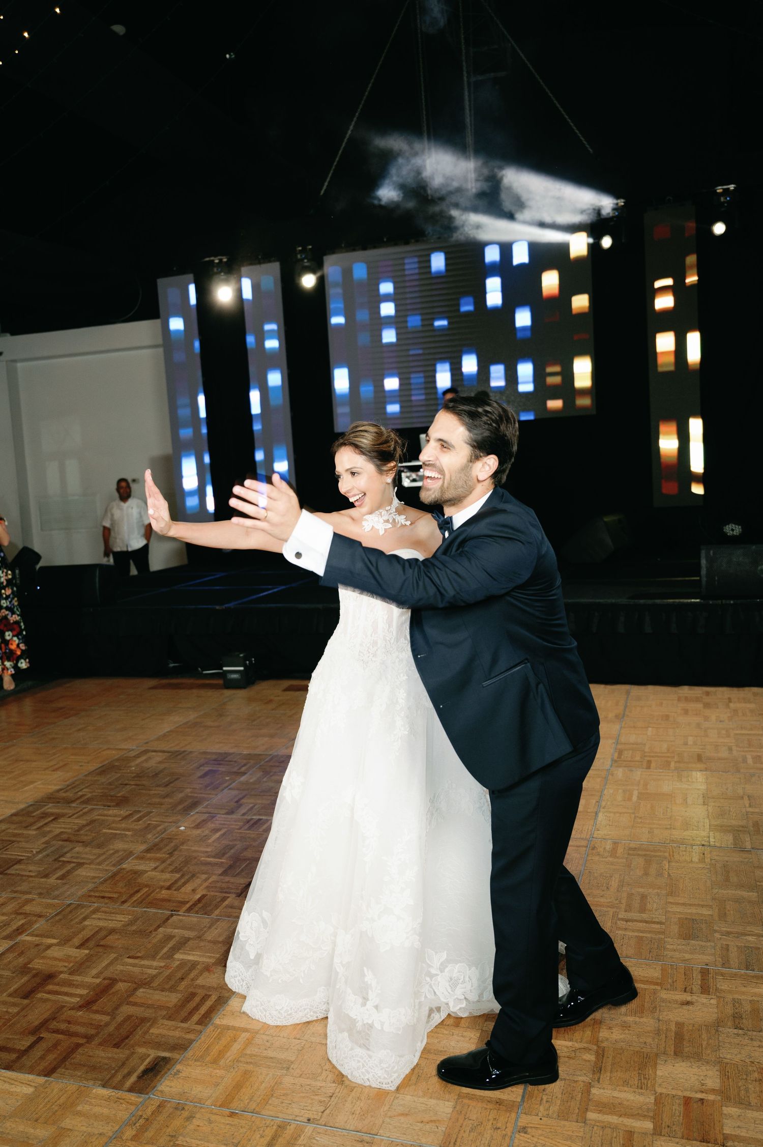 A couple performs a dramatic dip dance move on a wooden dance floor during a wedding reception.