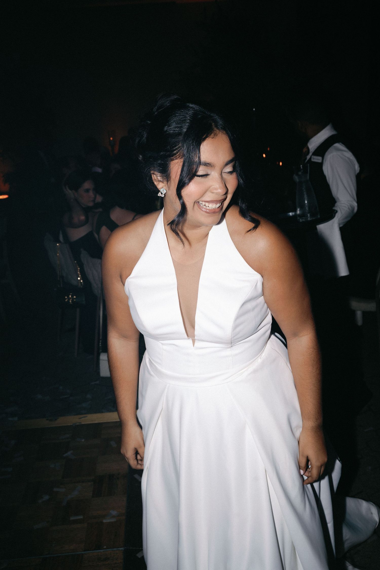 A person in a flowing white halter dress is shown dancing and enjoying themselves at a dark nighttime event.