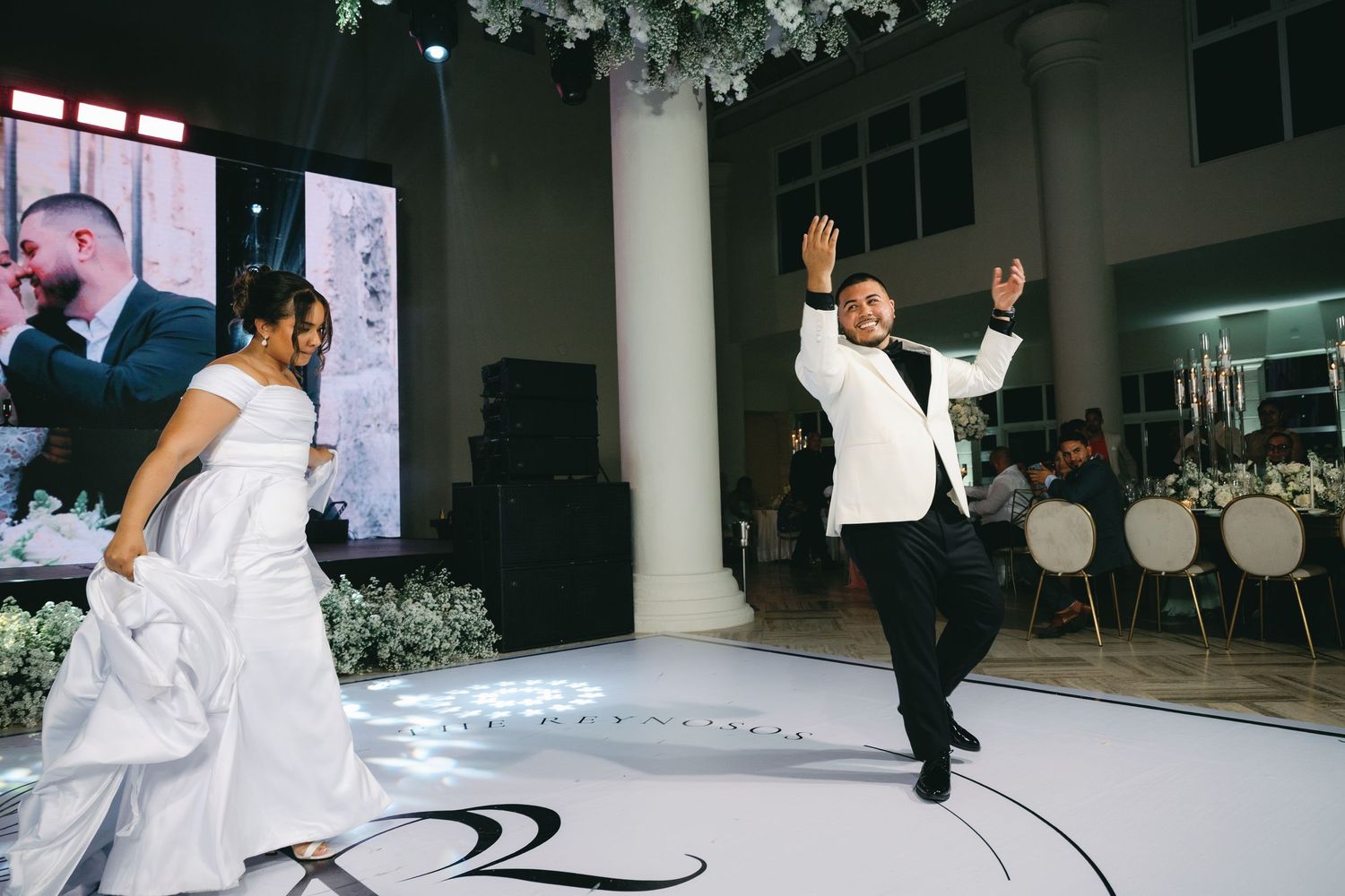 A couple celebrates joyfully during their first dance on a black and white patterned dance floor at their wedding reception.
