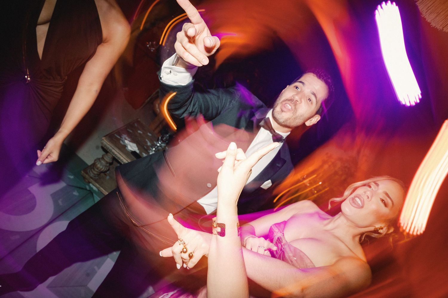 Party guests dance and celebrate with sparklers on a dance floor under colorful lighting at a nighttime event.