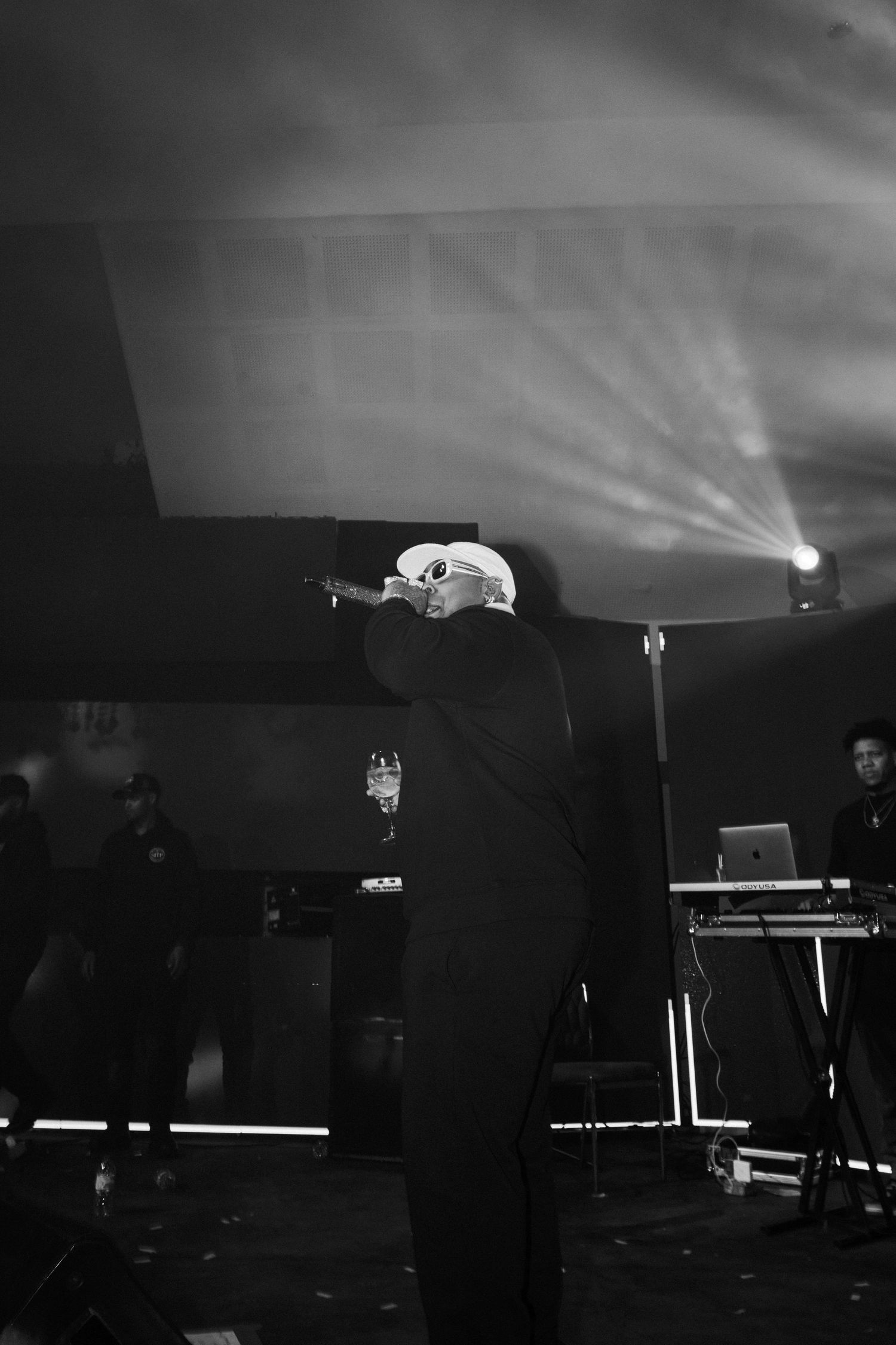 A performer in black silhouetted against dramatic stage lighting and beams during a concert performance.