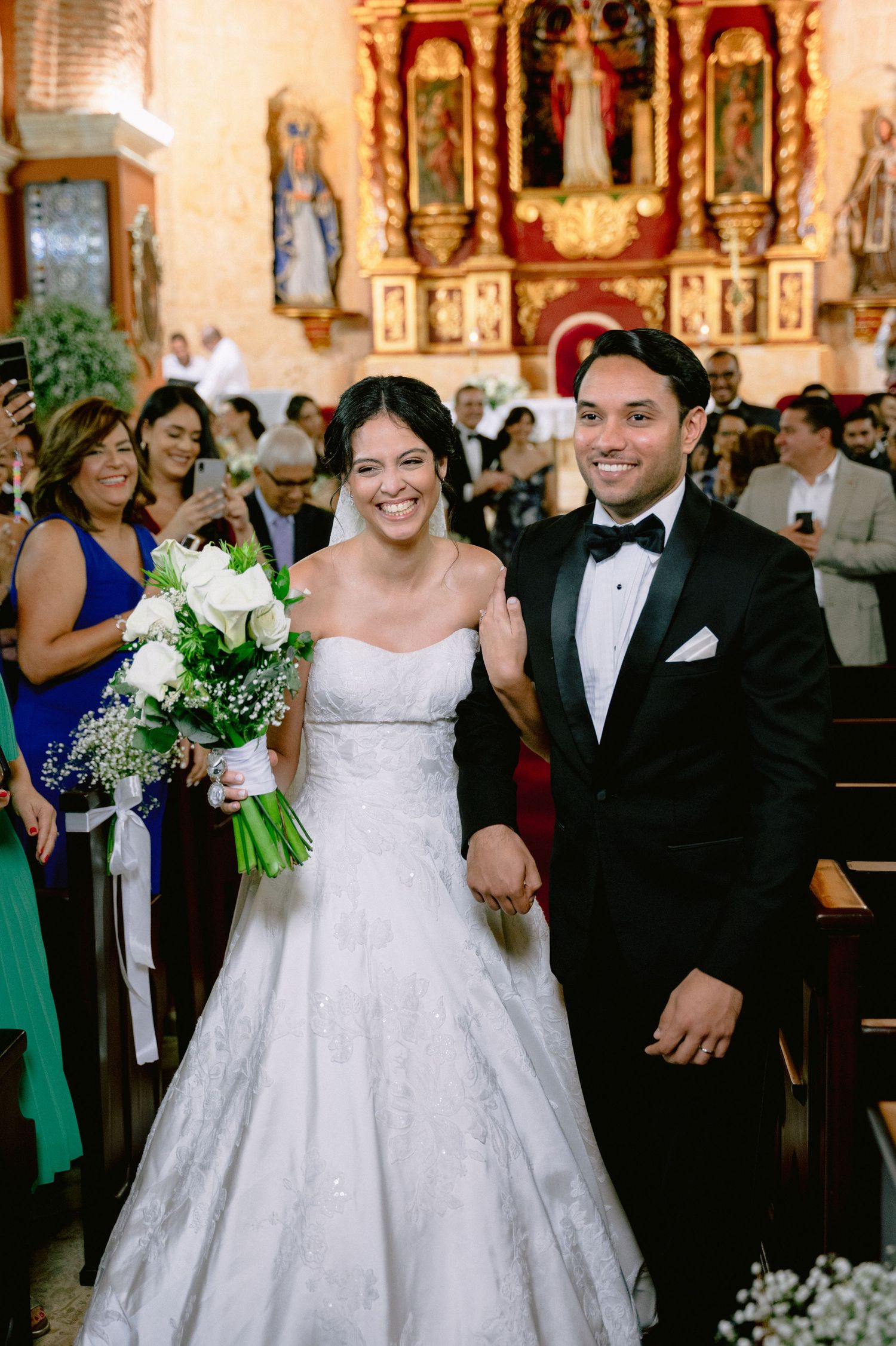 Joyful wedding procession down church aisle with bride in lace gown and groom in tuxedo.
