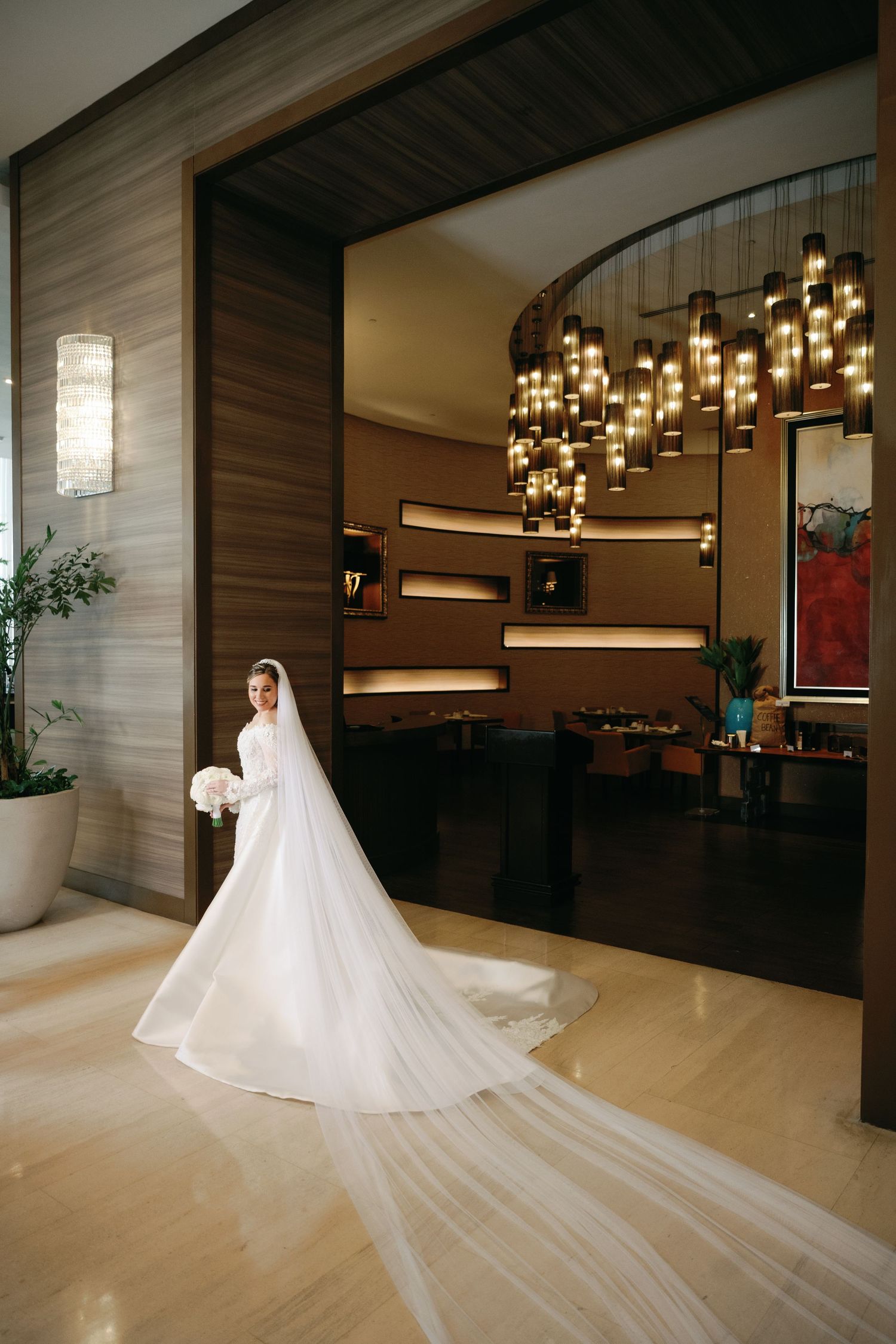 A flowing white wedding dress with a dramatic cathedral-length veil captured in a modern venue with warm lighting.