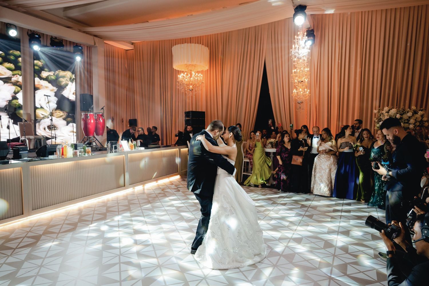 A couple shares their first dance on an illuminated dance floor at an elegant wedding reception with chandelier lighting.