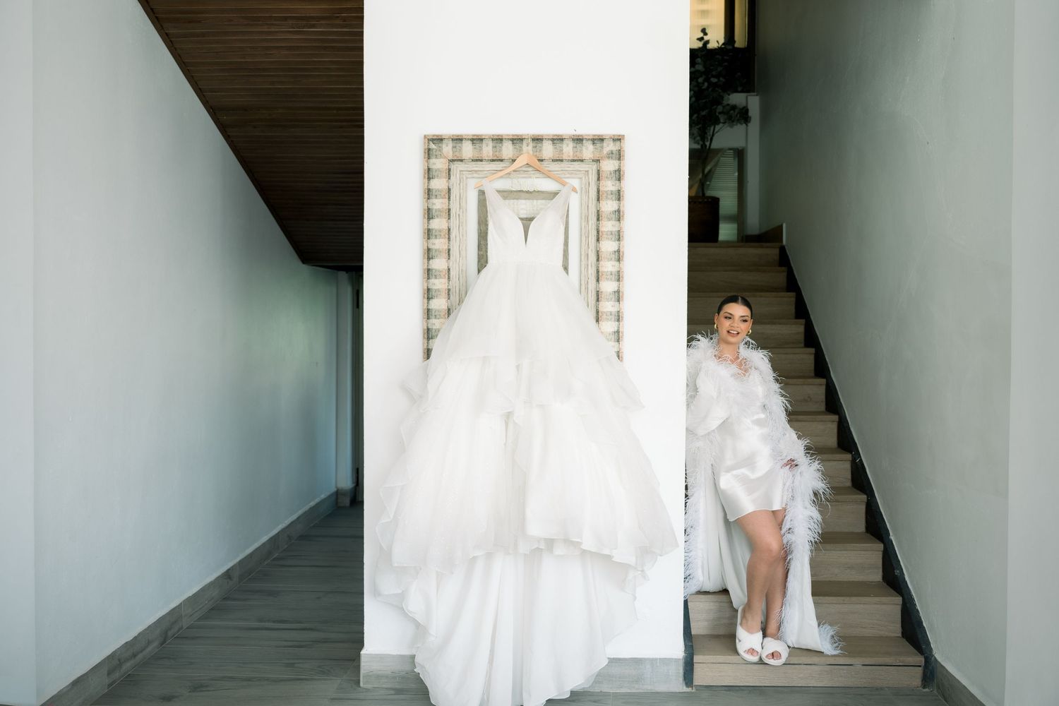 A white wedding dress hangs elegantly in a minimalist interior hallway.