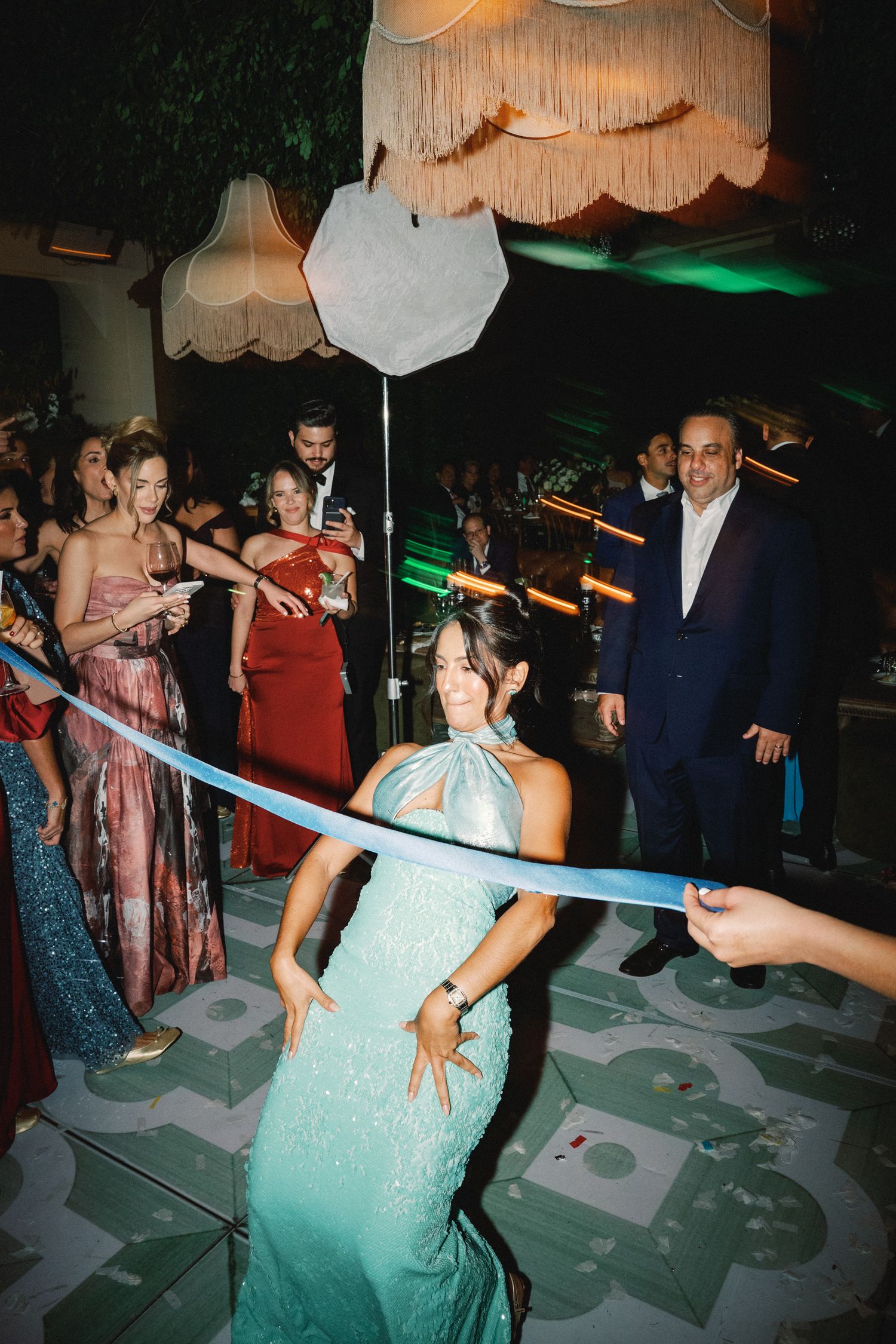 Partygoers dancing under decorative ceiling lights with a limbo bar in the center of the dance floor.