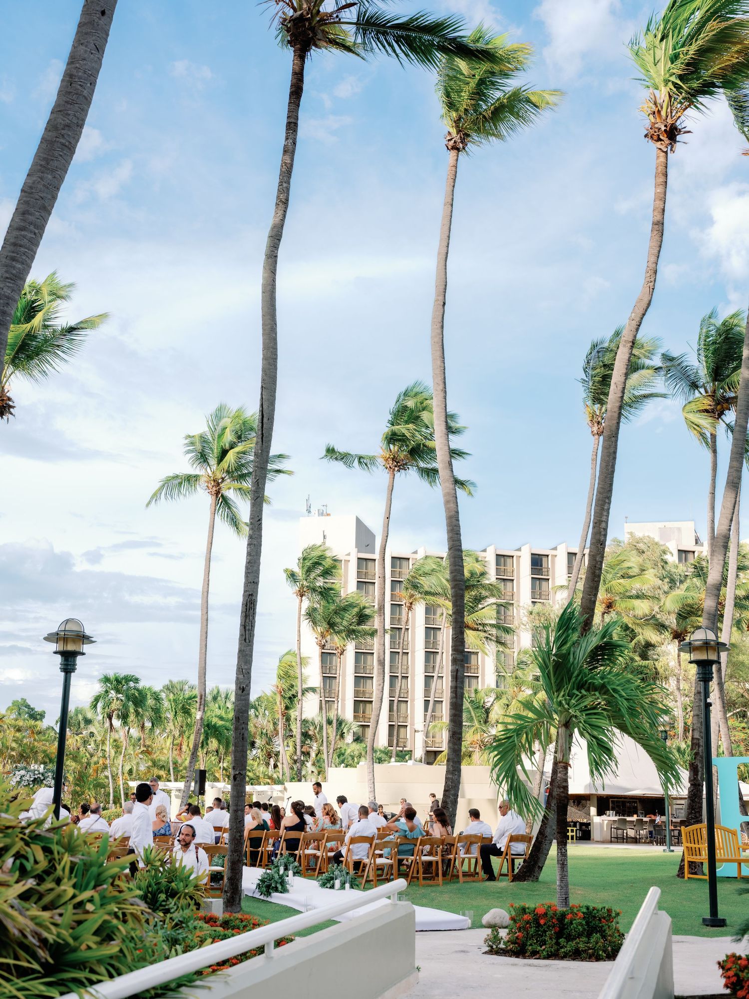 Palm tree lined outdoor venue with modern buildings and blue sky in a tropical resort setting.
