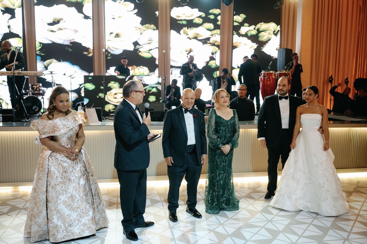 Wedding party members stand together during a formal reception in an elegant ballroom with decorative wall panels.