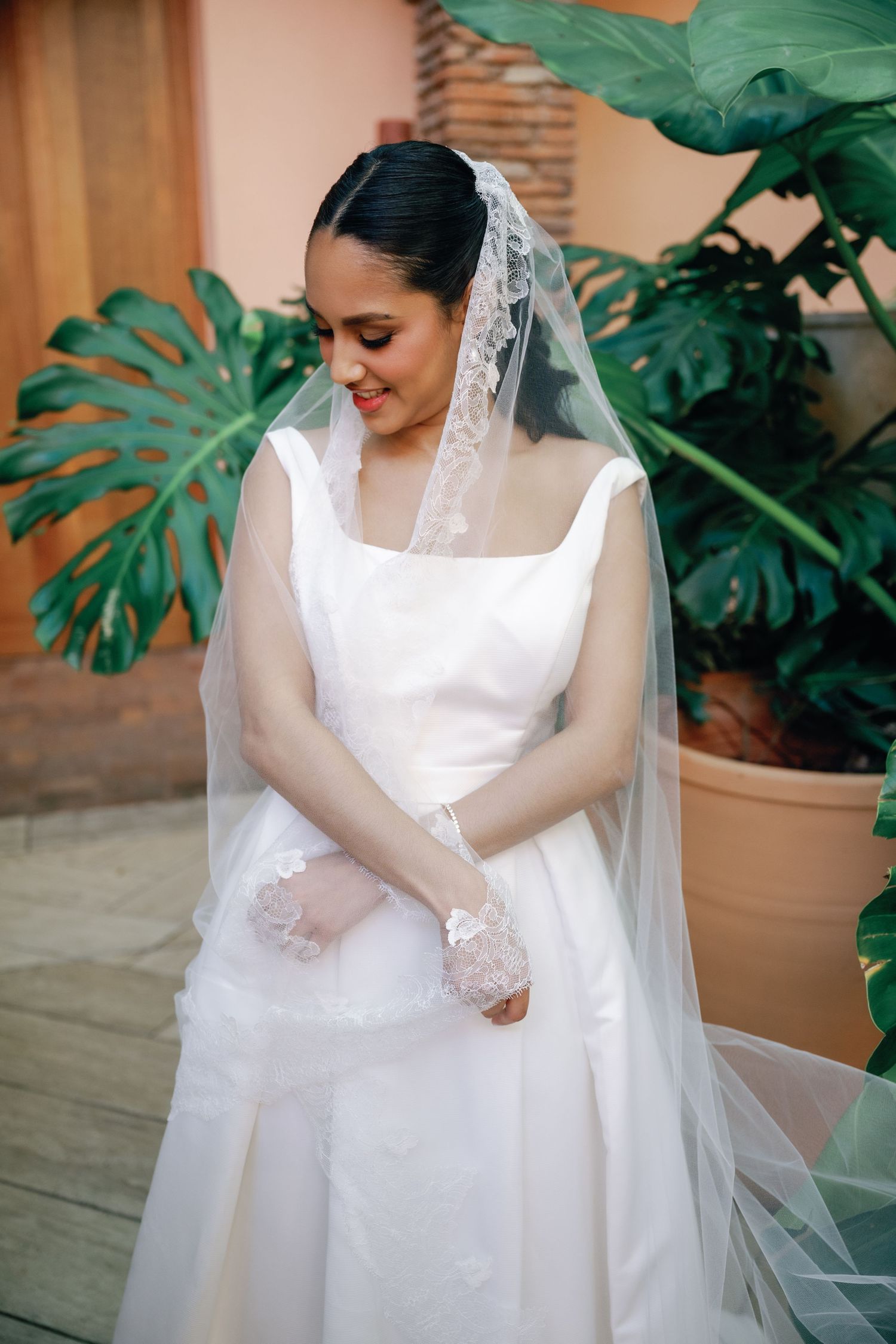 A flowing white wedding dress with delicate lace details photographed against tropical green foliage.