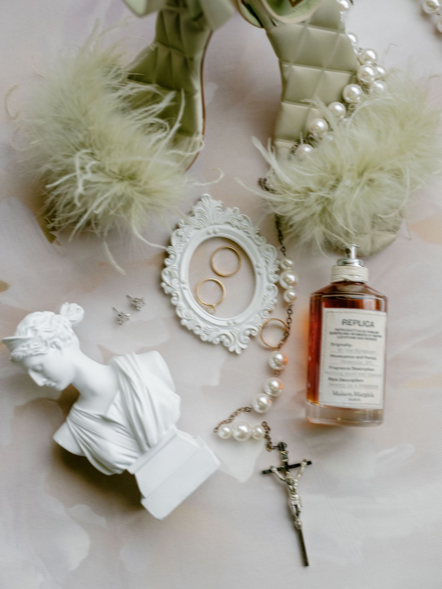 Wedding details arranged on white surface including perfume bottle, pearls, rings, and delicate white floral elements.