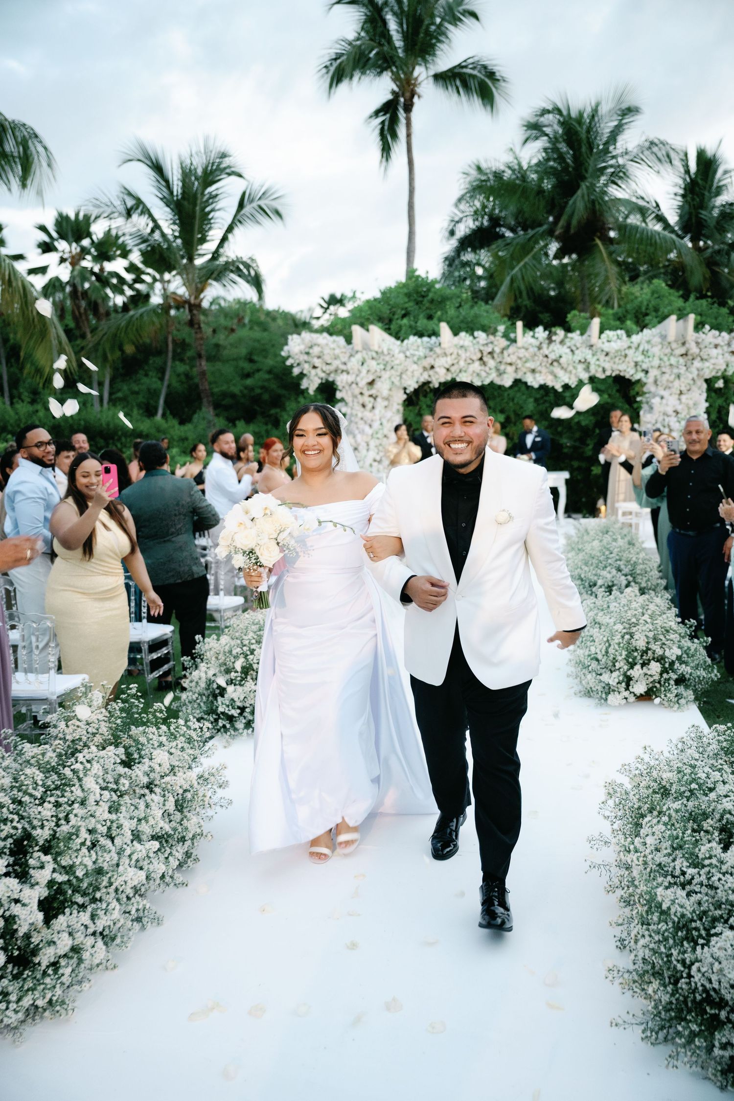 A wedding ceremony aisle lined with delicate baby's breath flowers and palm trees in a tropical outdoor setting.