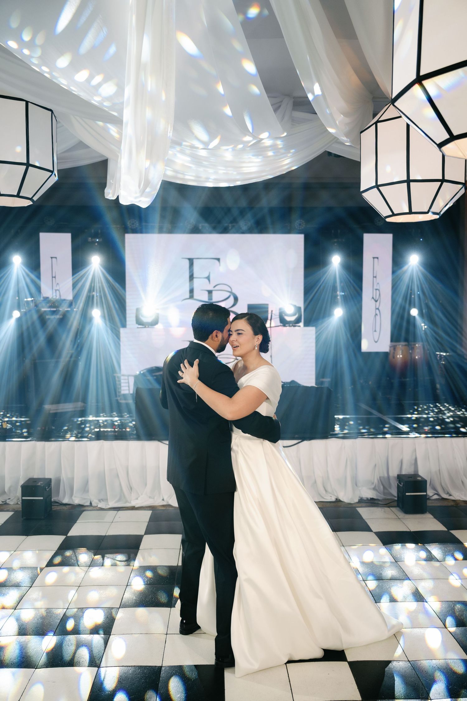 Couple sharing their first dance at a wedding reception with dramatic lighting and geometric lanterns overhead.