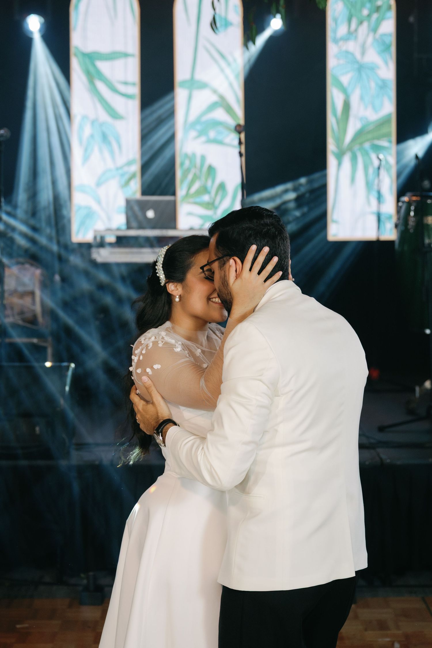 A romantic first dance between newlyweds in white attire against a backdrop of illuminated panels.
