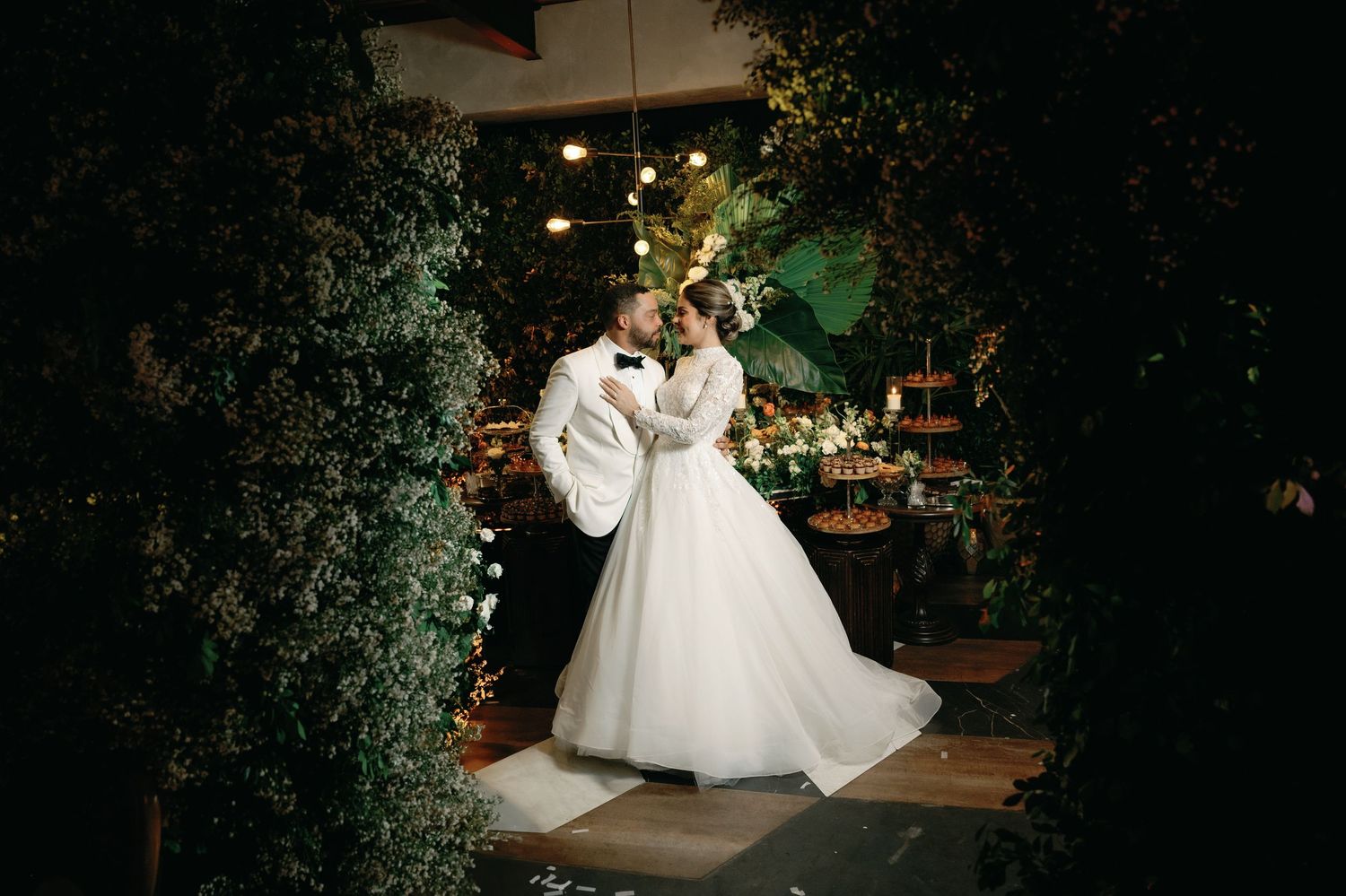 A bride in a flowing white gown twirls gracefully in a dimly lit outdoor garden setting.