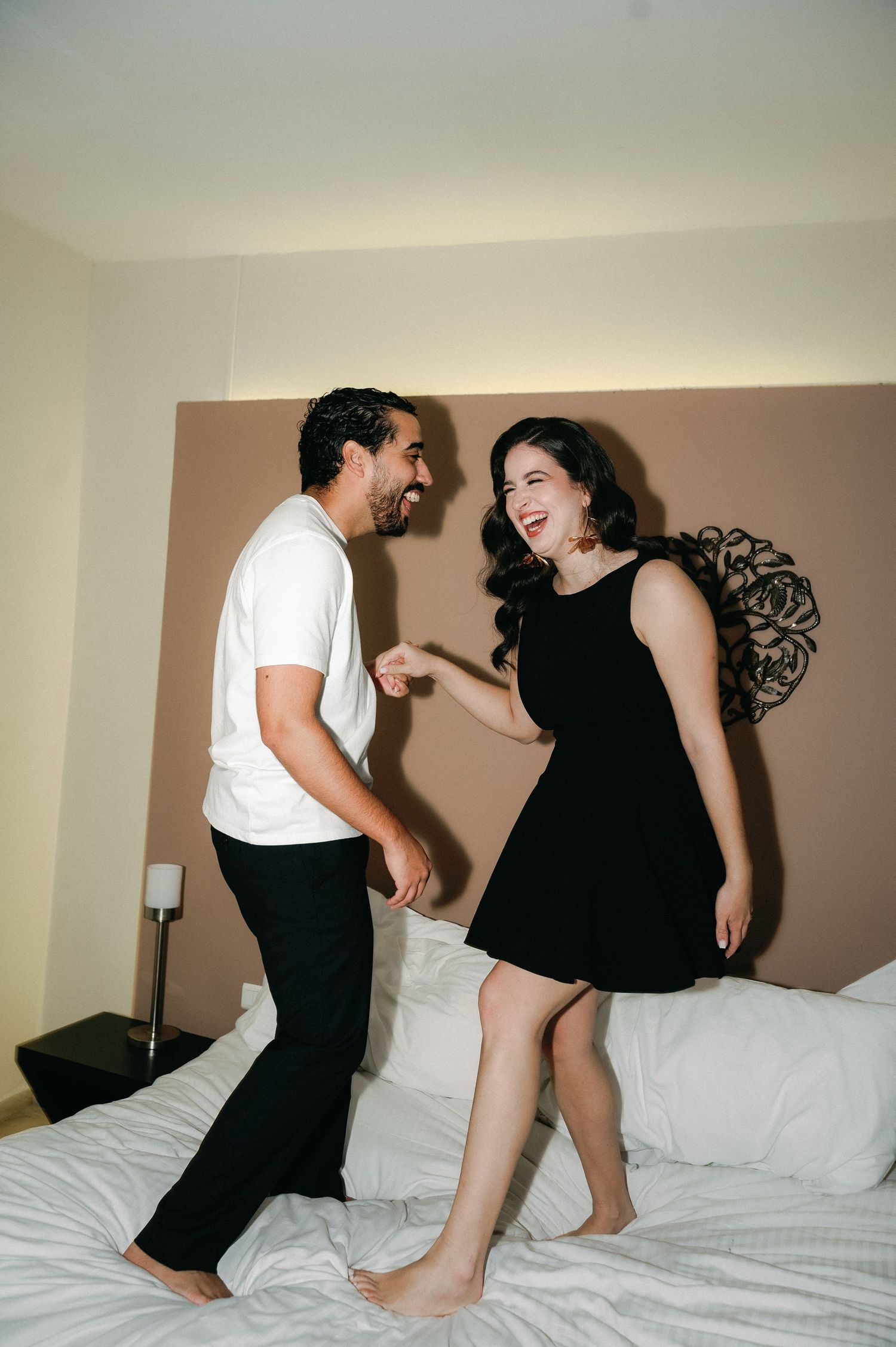 A couple in black and white outfits playfully interacting on a white bed in a sequence of candid shots.