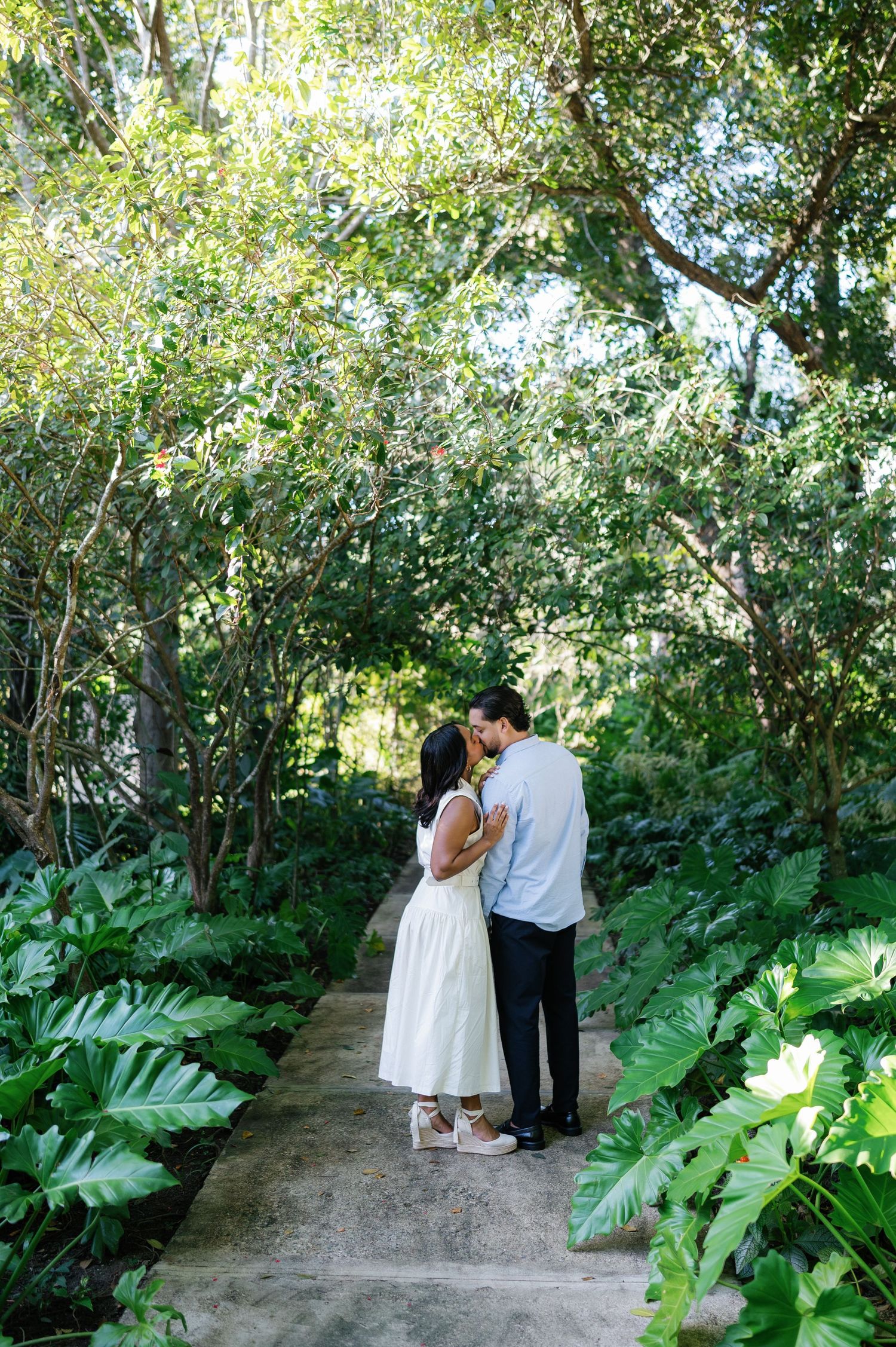 A couple walks together on a garden path surrounded by lush tropical foliage and greenery.