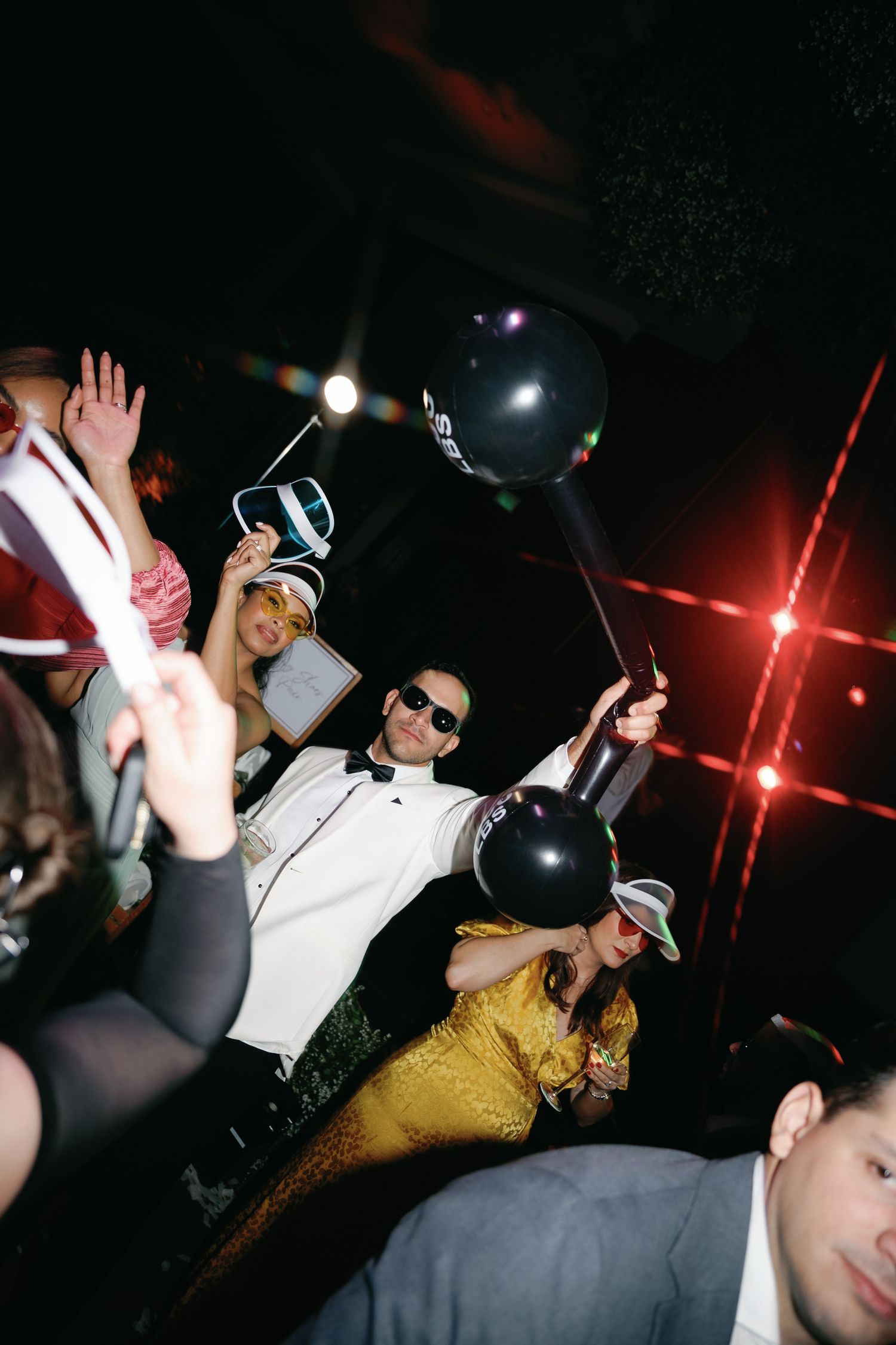 People dancing and partying in a dimly lit nightclub with black balloons and red lighting effects.