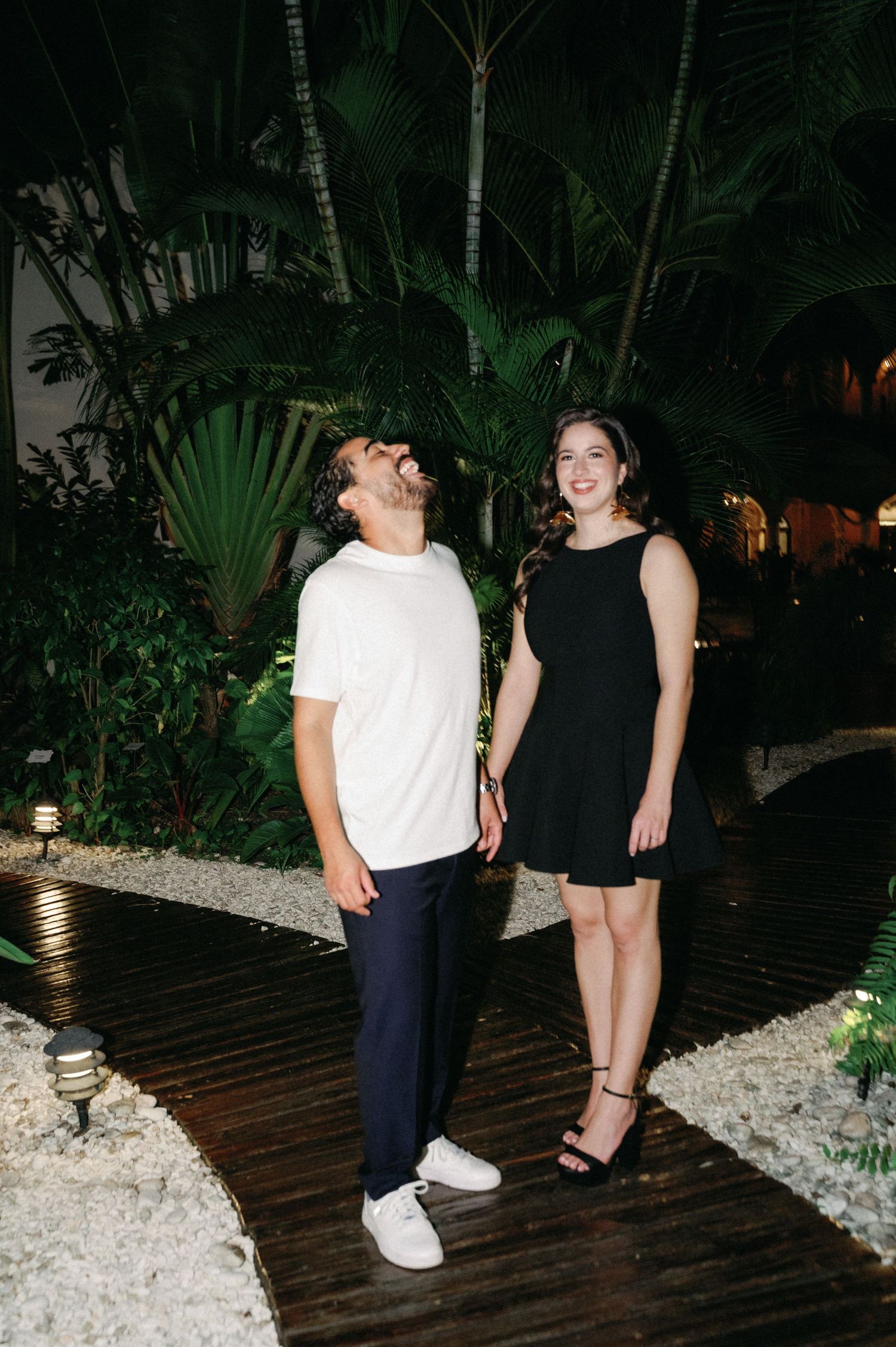 A couple shares a romantic moment on a wooden deck surrounded by tropical plants at night.