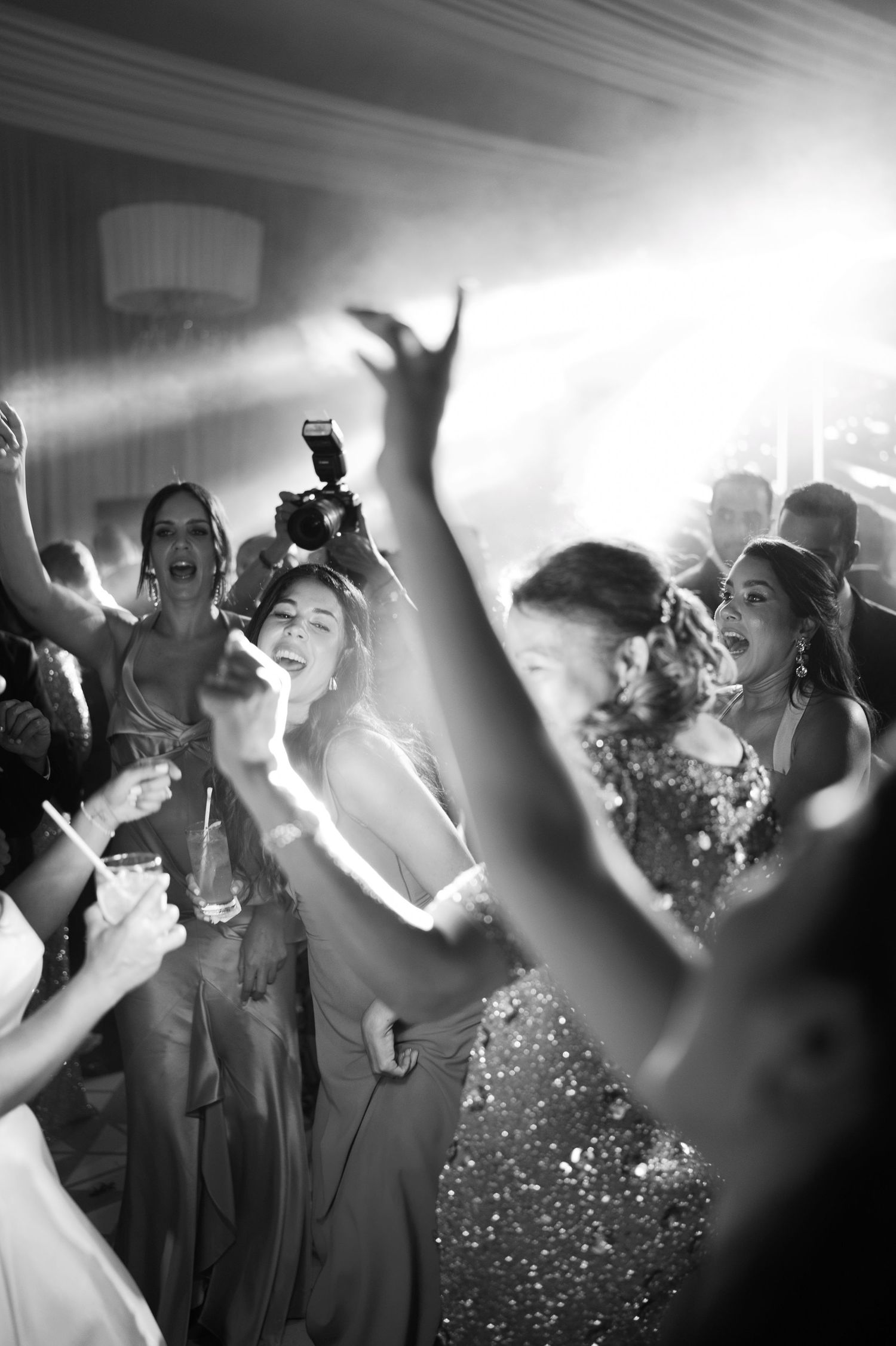 Black and white photo of people dancing and celebrating at a party with dramatic lighting and raised hands.
