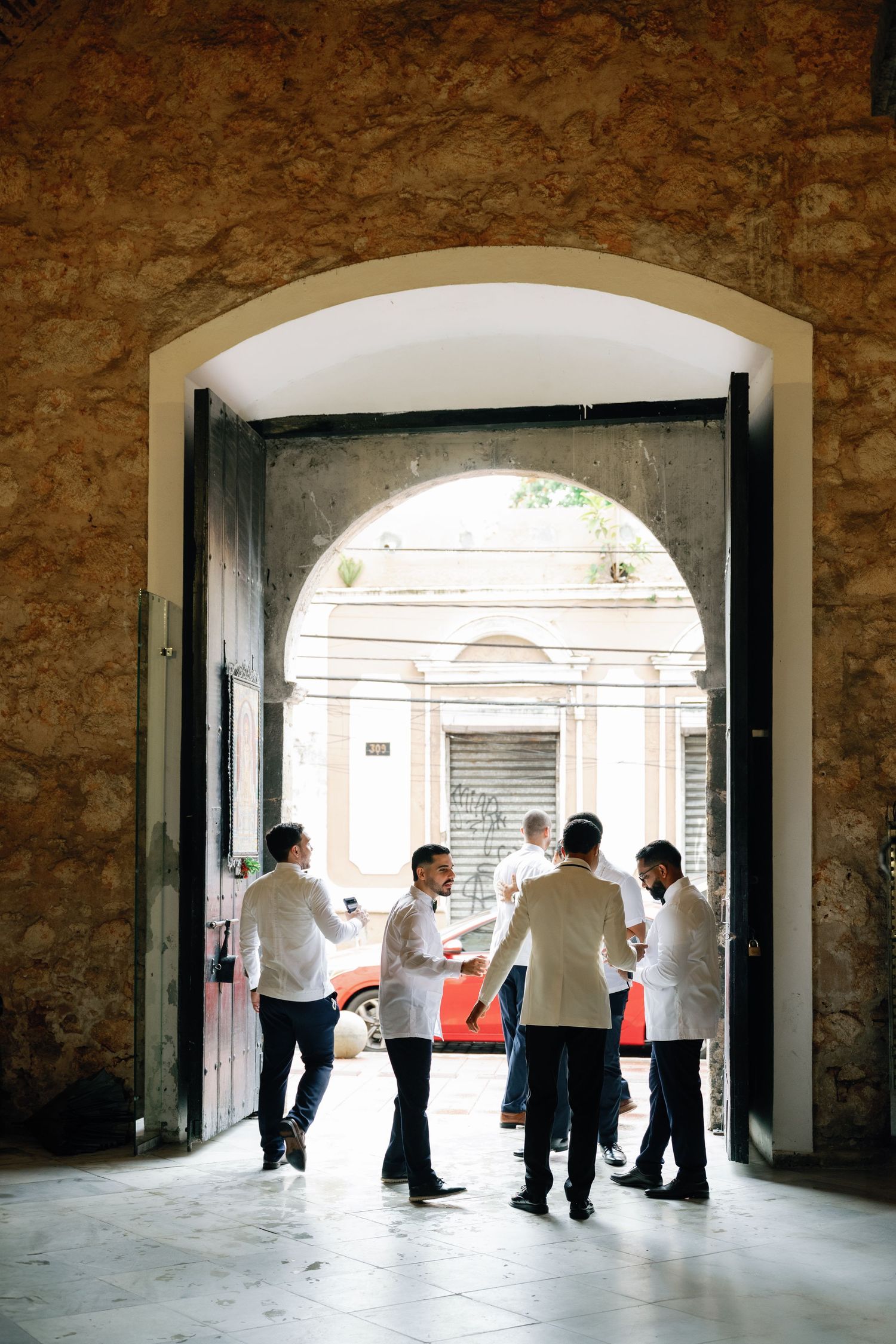 A group of people standing in a stone archway entrance having a conversation in natural light.