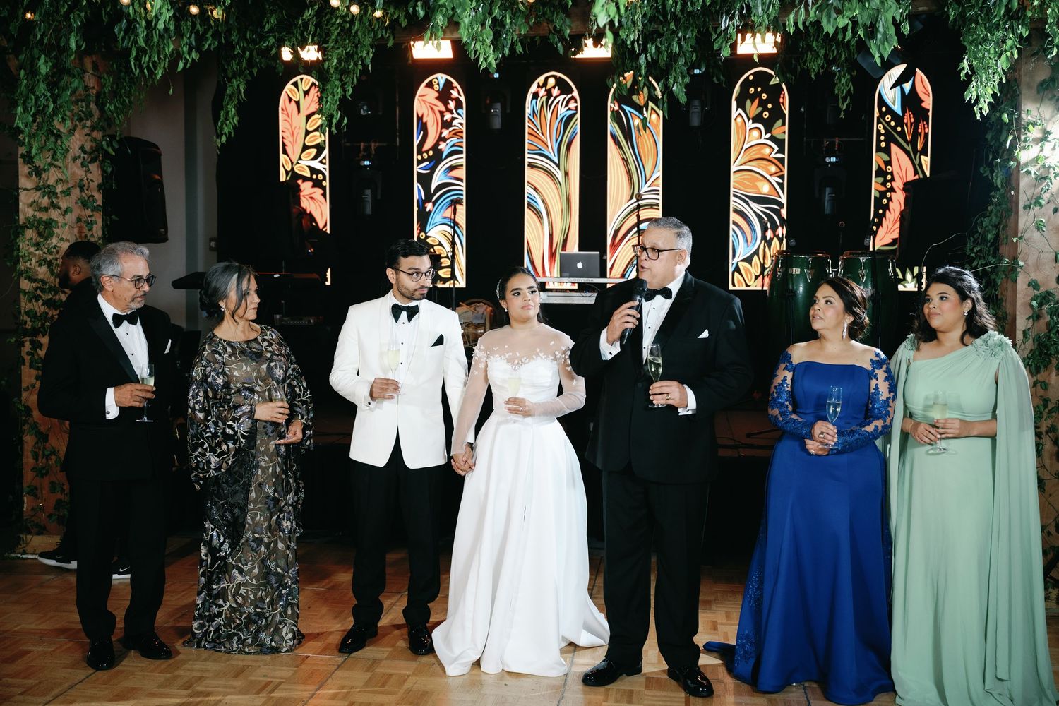 Wedding party members in formal attire stand together in a line against a dark background.