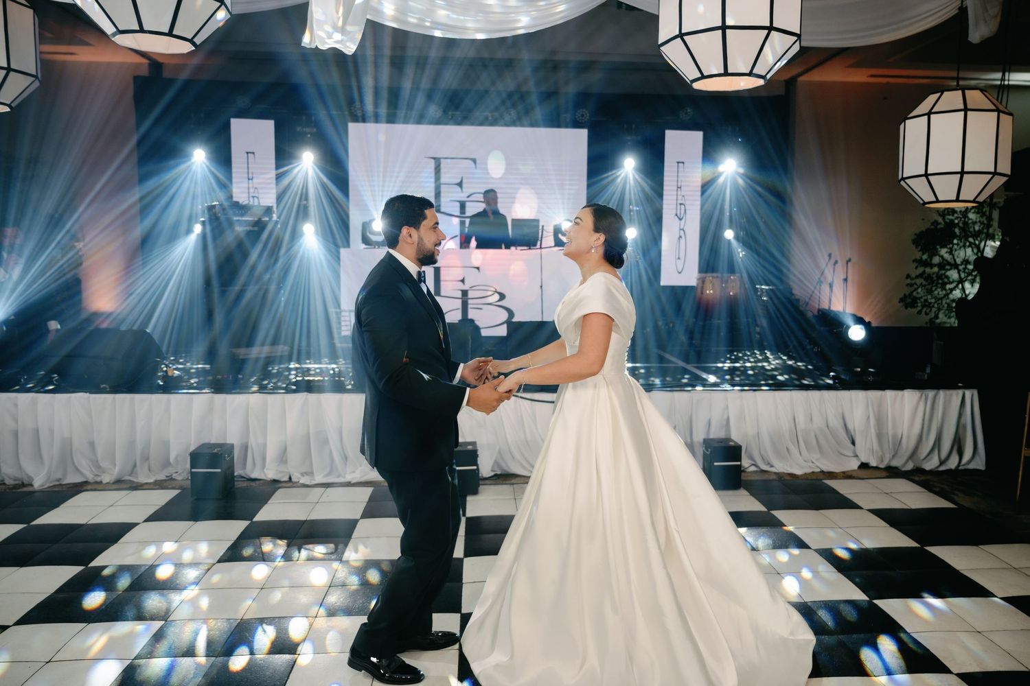 A couple shares their first dance on a black and white checkered dance floor at an elegant wedding reception.