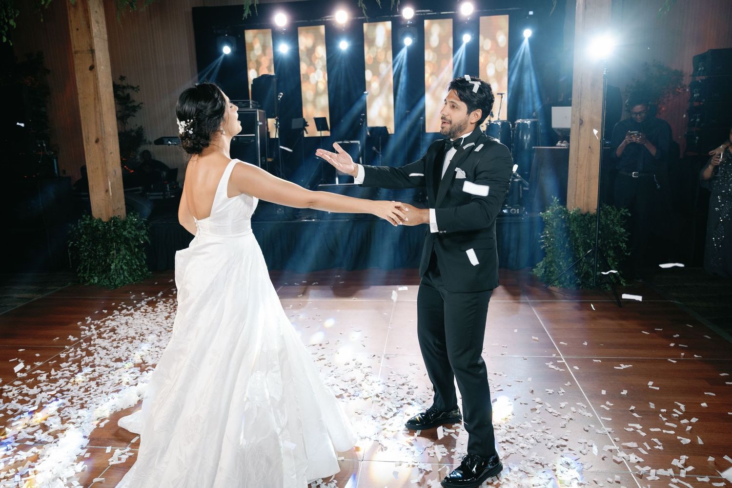 A couple shares their first dance at a wedding reception as confetti falls around them on the dance floor.