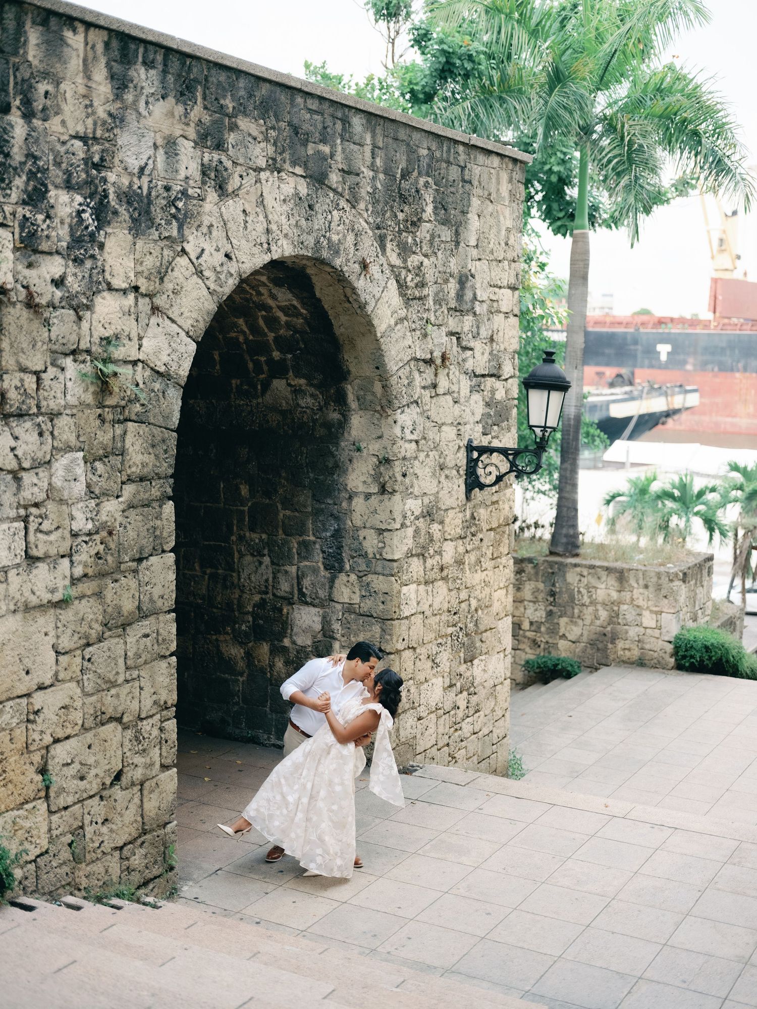 A stone archway passage with palm trees visible in an old colonial style architecture setting.
