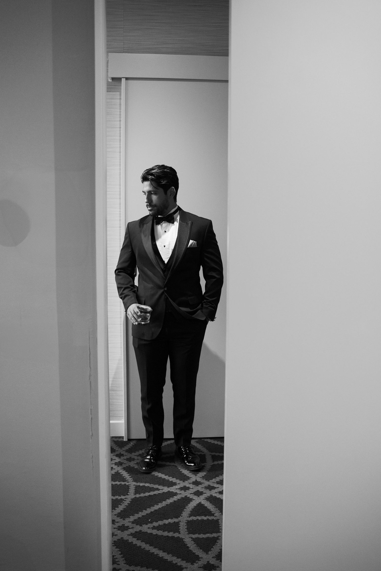 A black and white photo series showing a person in a formal black suit standing against a white wall.