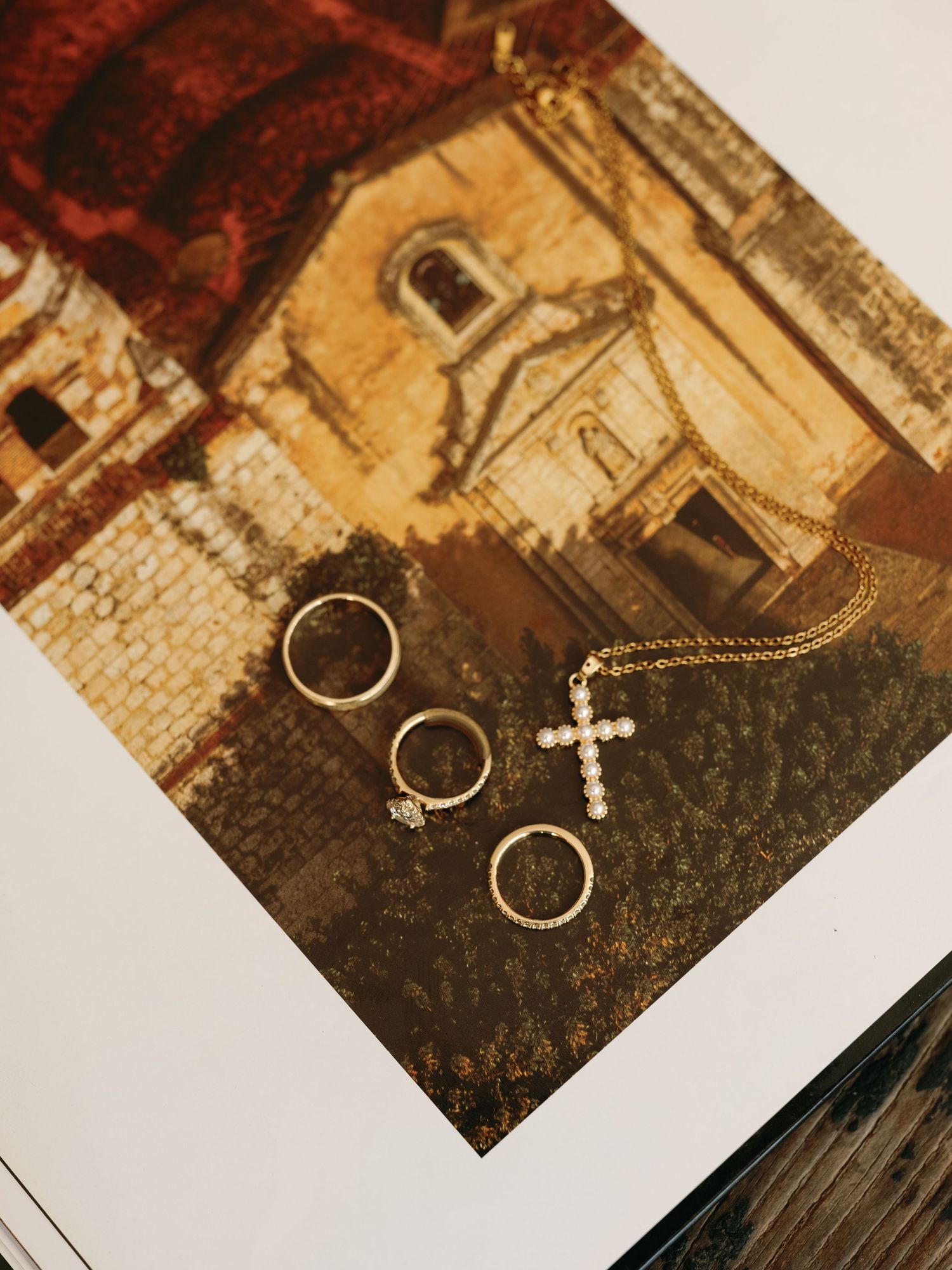 Wedding rings and cross necklace arranged on vintage textured paper in warm sepia tones create an artistic detail shot.
