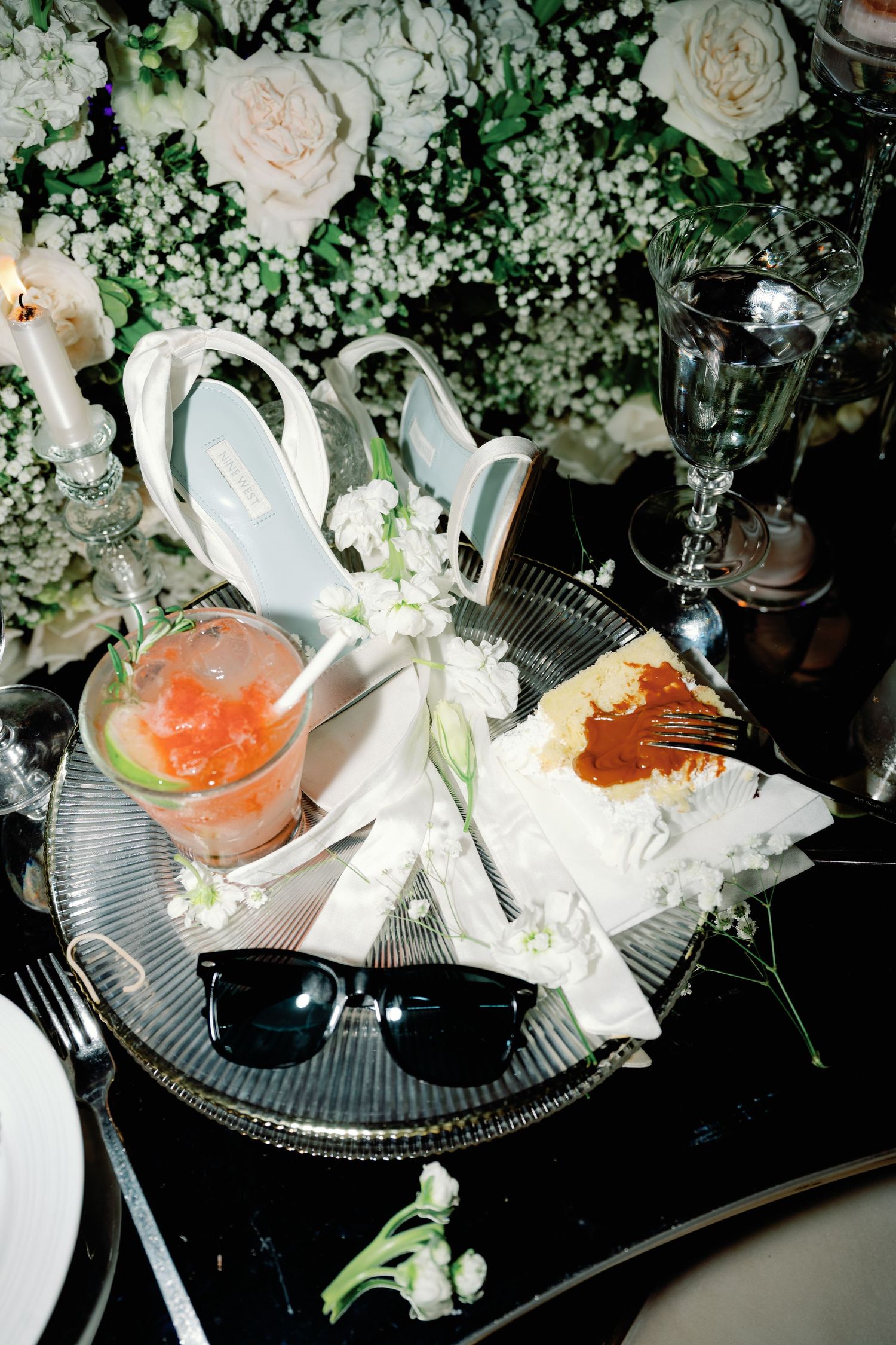 Elegant place setting with white flowers and orange cocktail on dark surface with decorative floral arrangements.