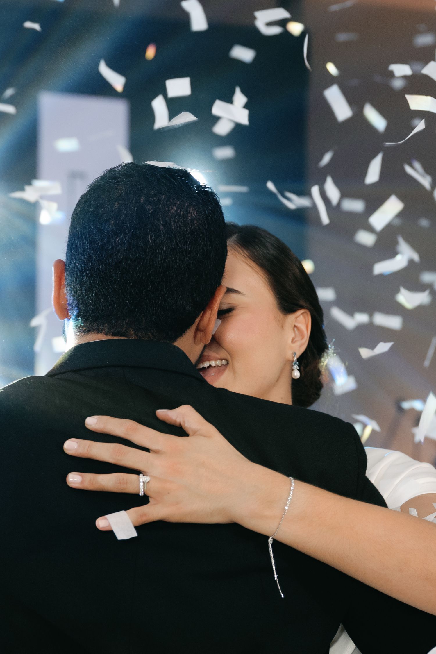 Couple embracing during celebration with white confetti falling in dark room with blue lighting.