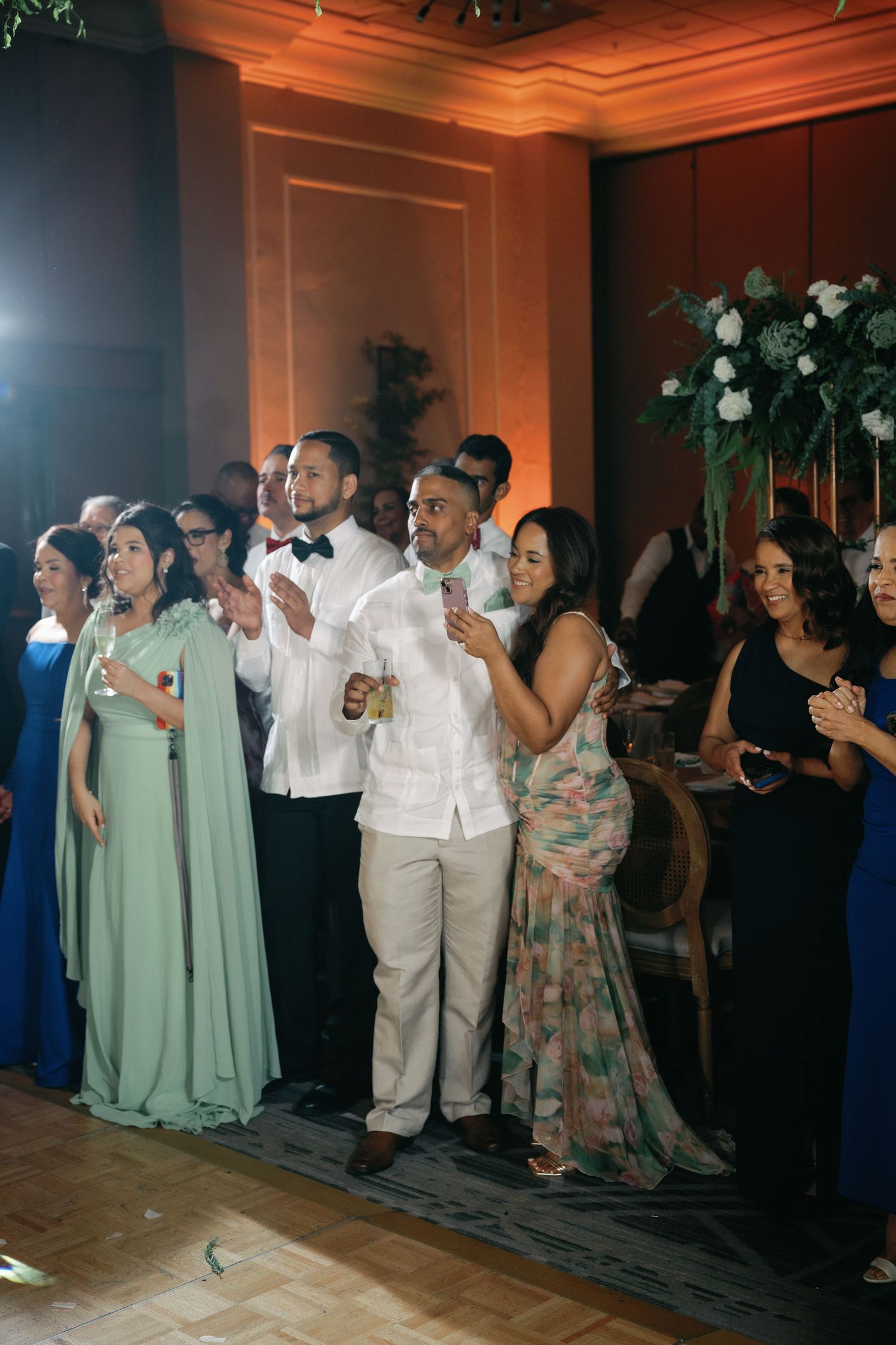 Wedding party and guests in mint green dresses and formal attire dancing in a line at the reception.