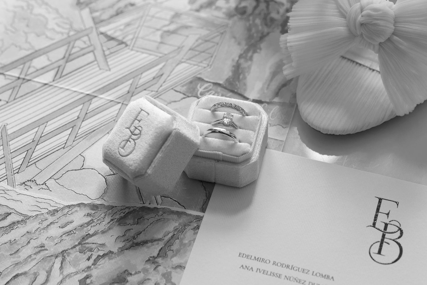 Black and white image of hands working on architectural drawings and sketches spread across a desk surface.
