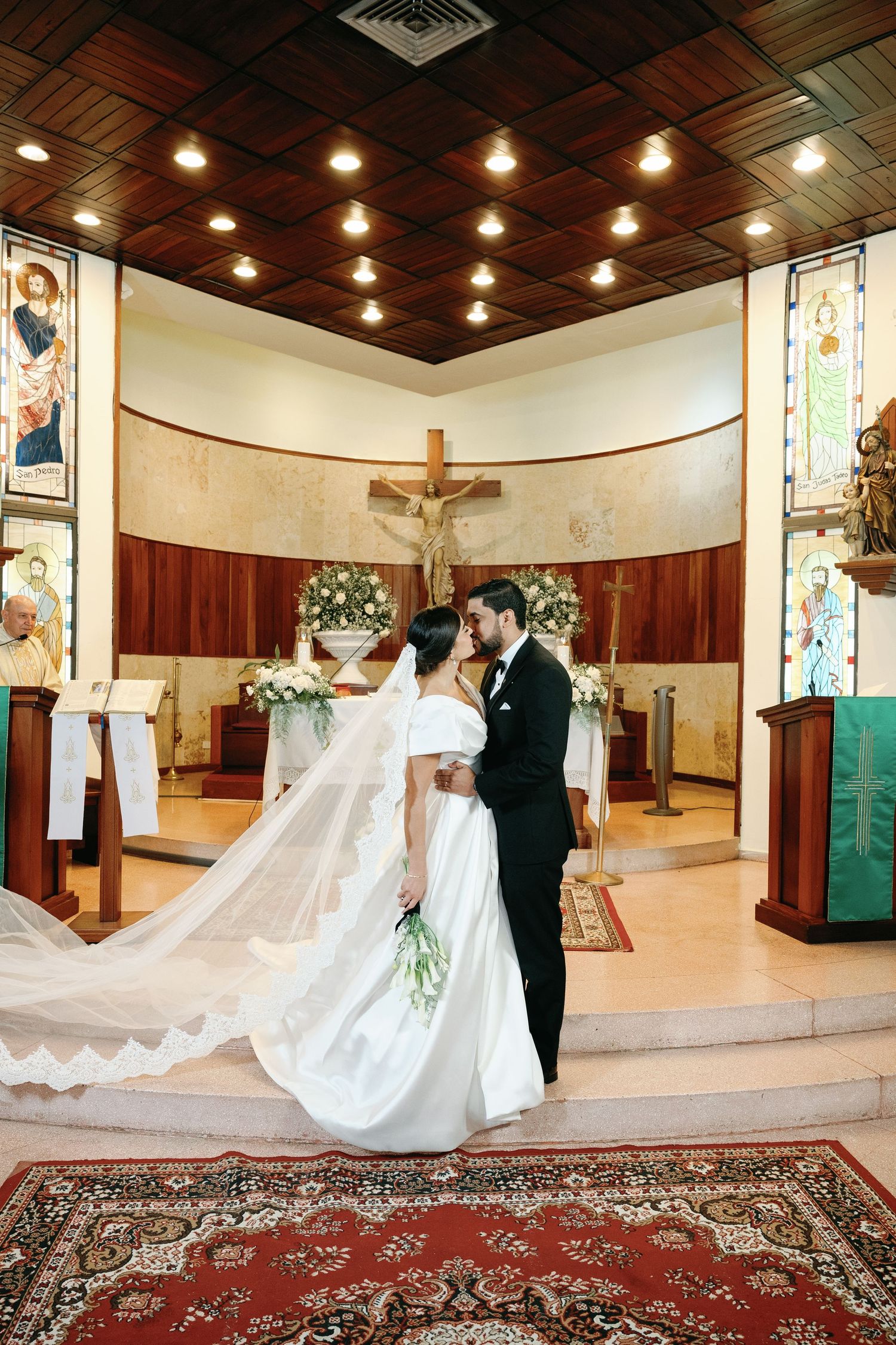Elegant wedding couple poses in a church sanctuary with dramatic flowing veil and ornate carpet details.