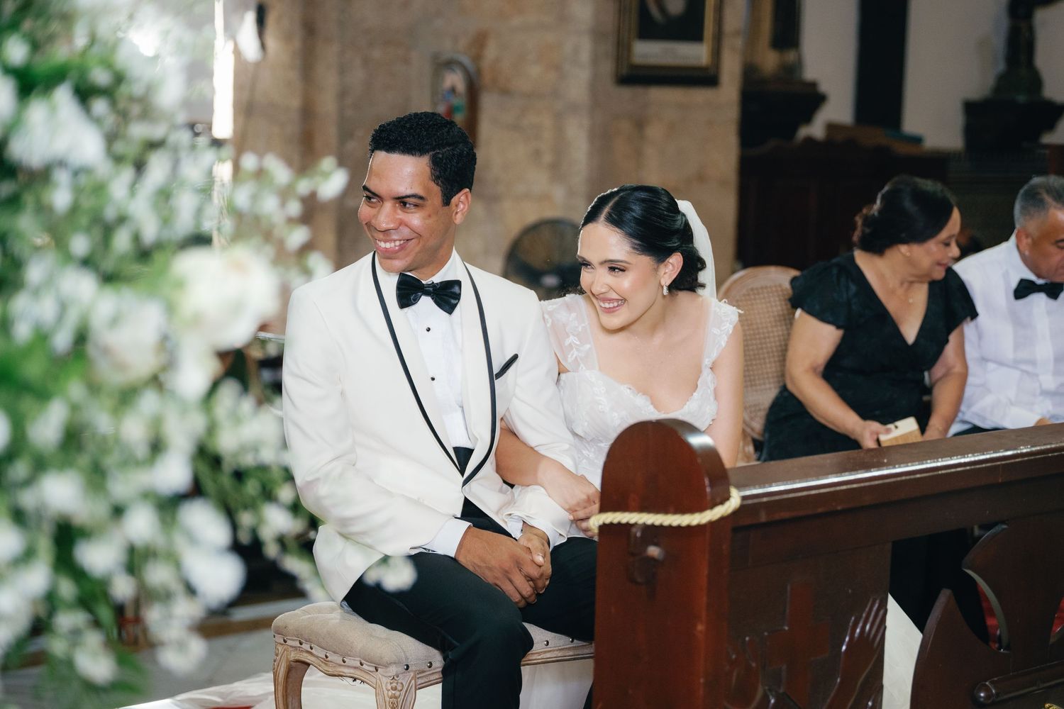 A couple sits together on wooden church pews during a formal ceremony.