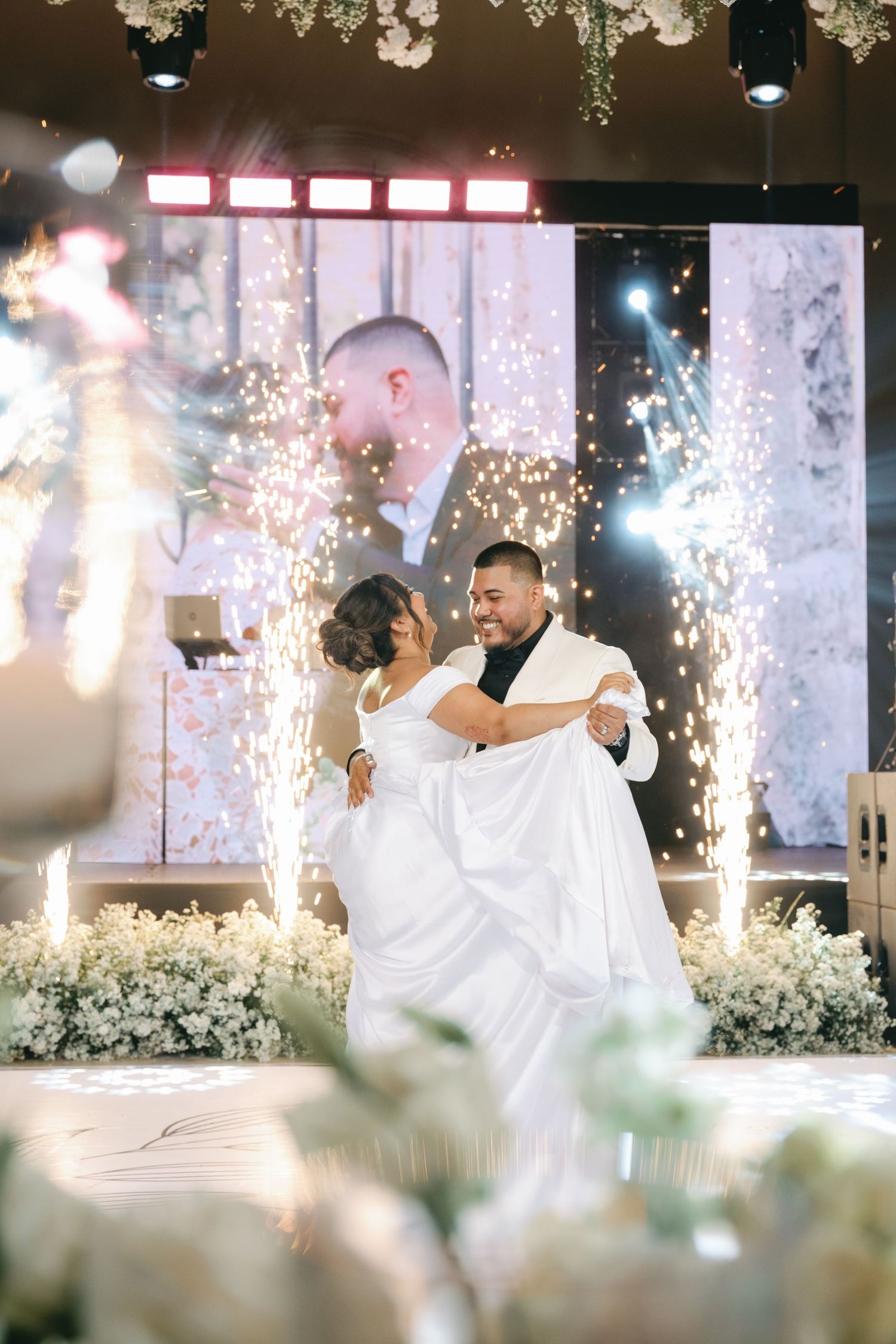 A couple shares their first dance surrounded by sparklers and floral decor at an elegant wedding reception.