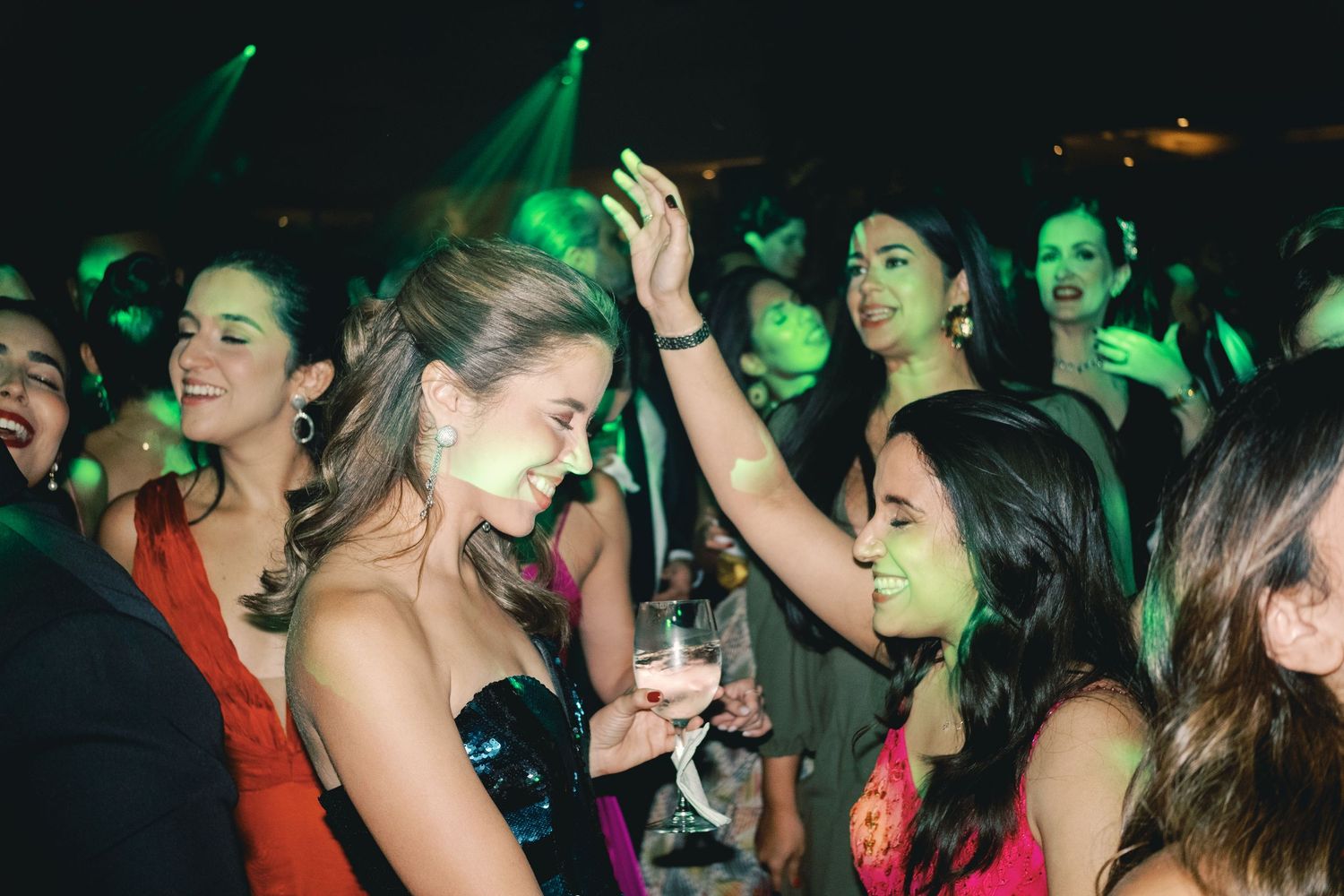Crowd of people dancing and celebrating at a nightclub with green lighting effects.