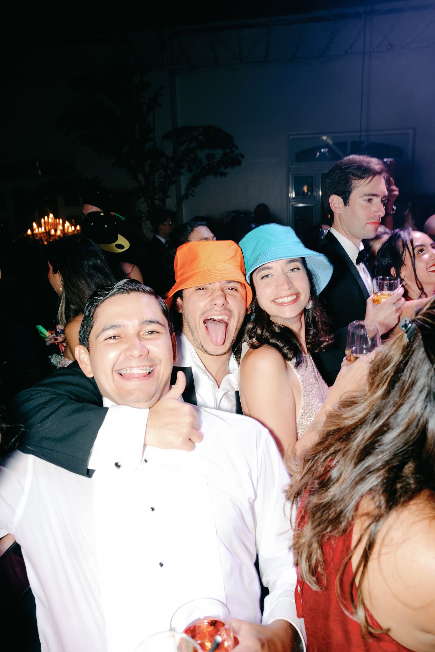Party guests wearing colorful beanies and formal attire celebrate together at a lively indoor event.