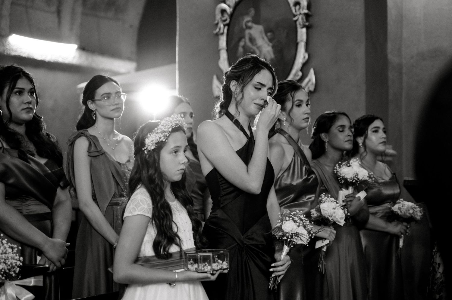 A black and white photograph of a wedding party watching an emotional moment during the ceremony.