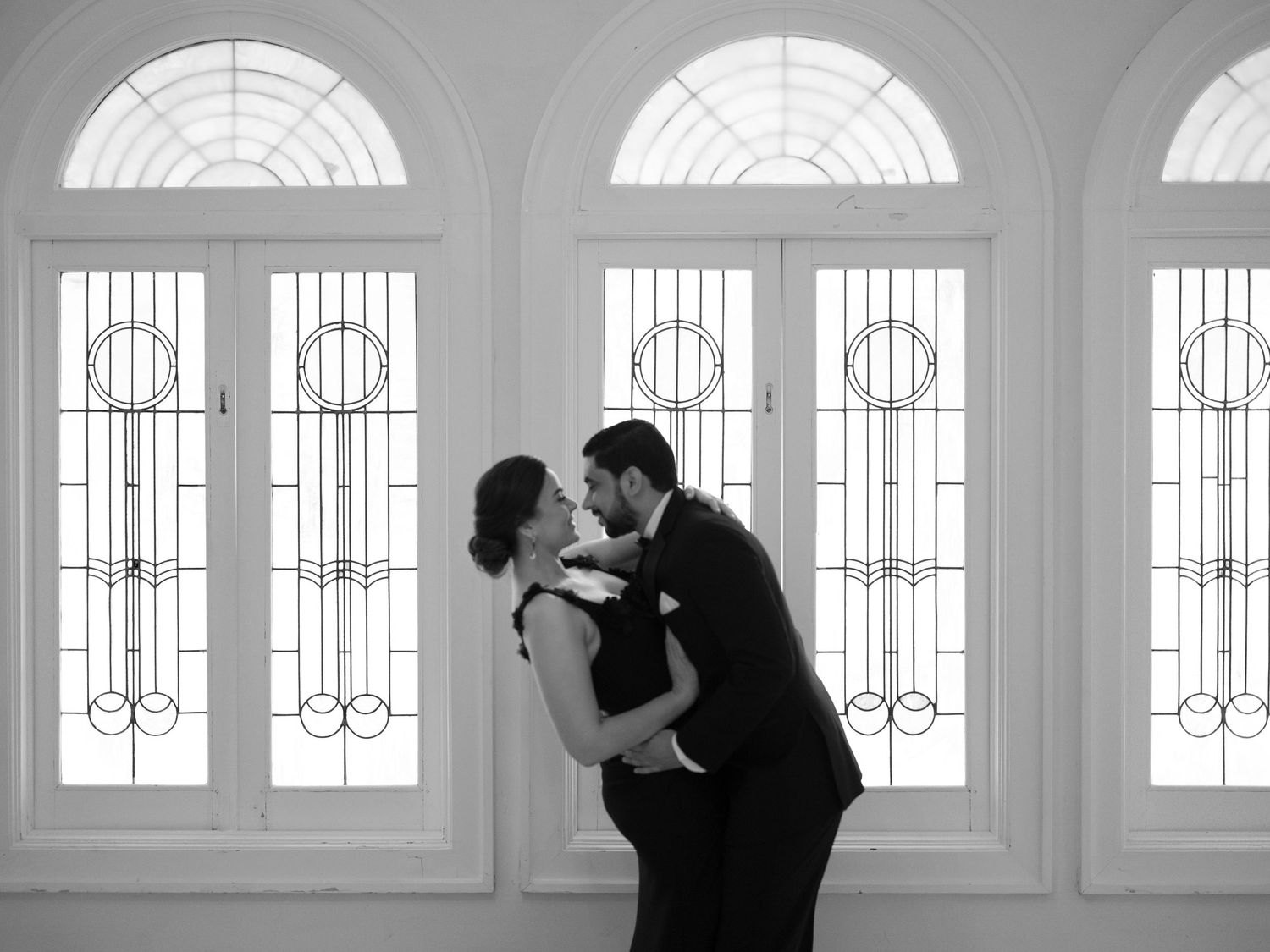 Silhouettes of a dancing couple against bright windows in an elegant interior space.
