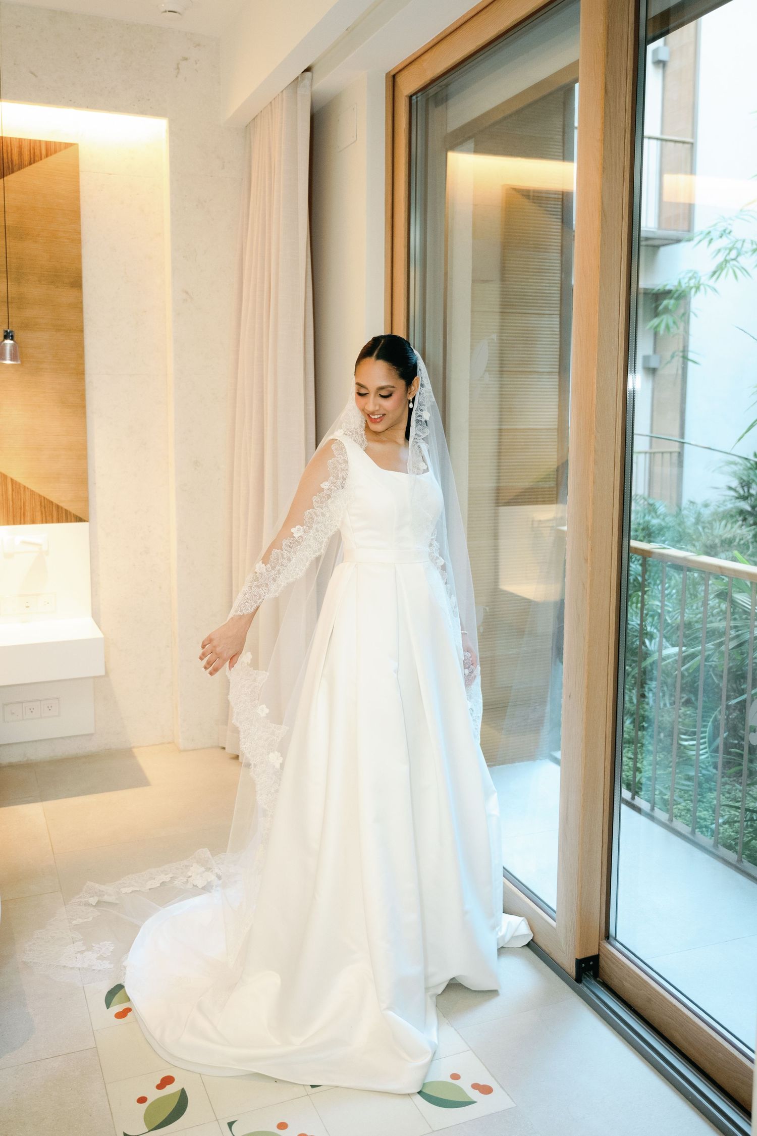 Elegant white wedding dress with flowing train photographed in a bright modern room with large windows.
