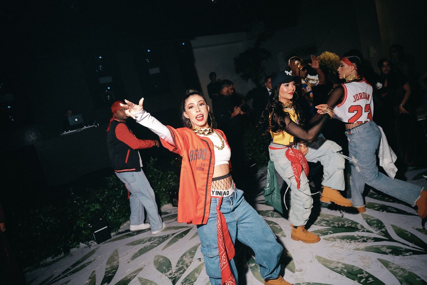Enthusiastic dancers in casual and formal wear perform on a white-covered dance floor at night.