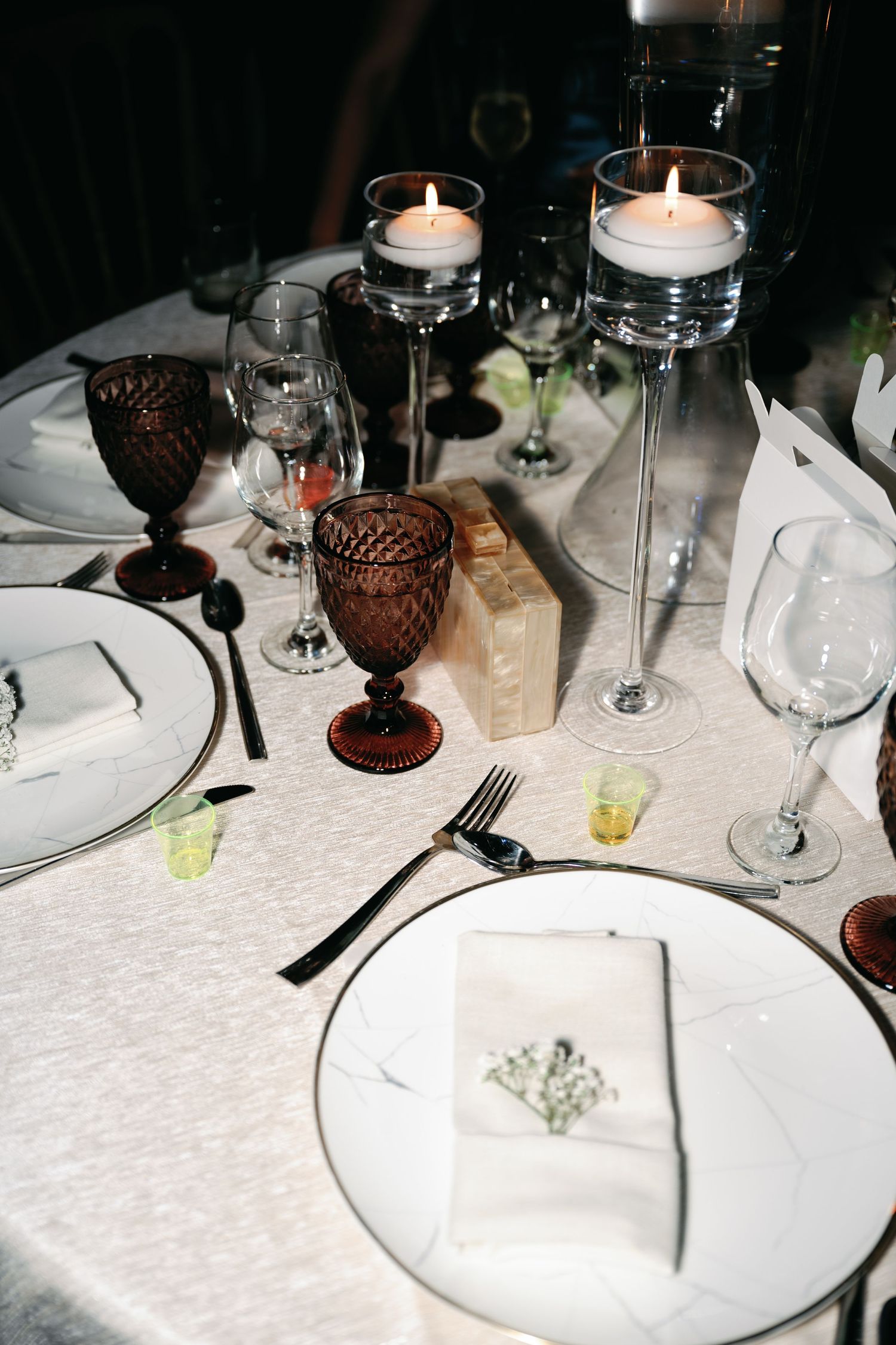 Elegant table settings with white linens, crystal glassware, and amber-colored stemware create an intimate dining atmosphere.