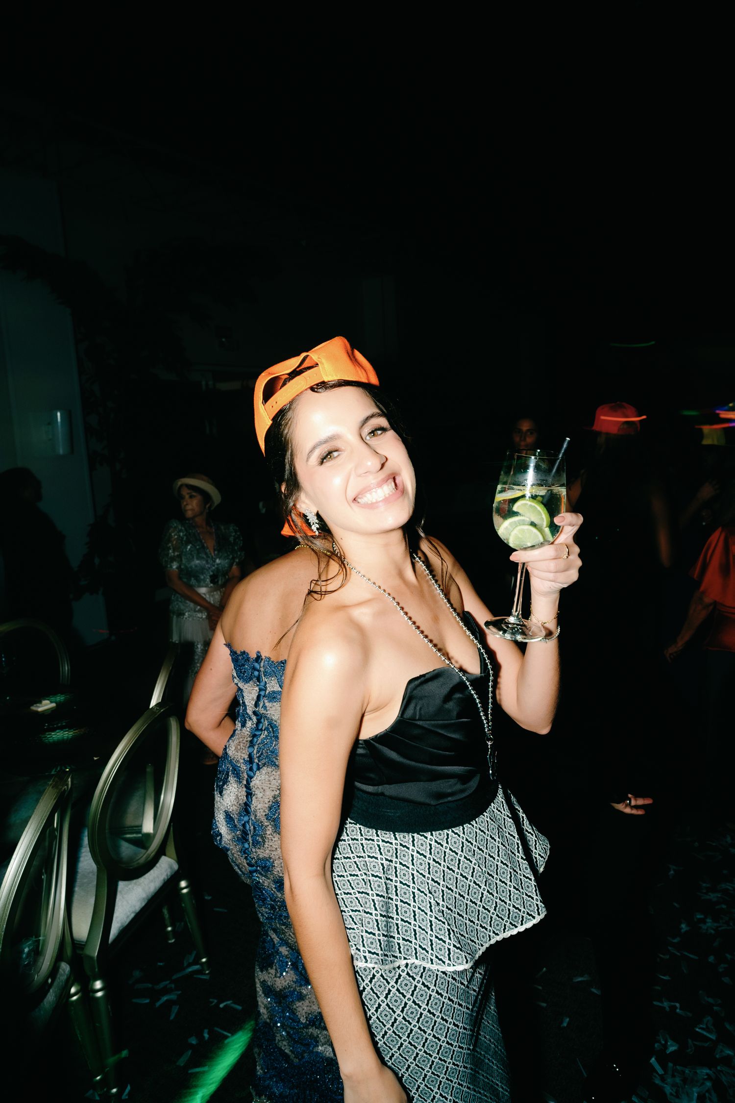 Party scene with people dancing and holding drinks under dim lighting.