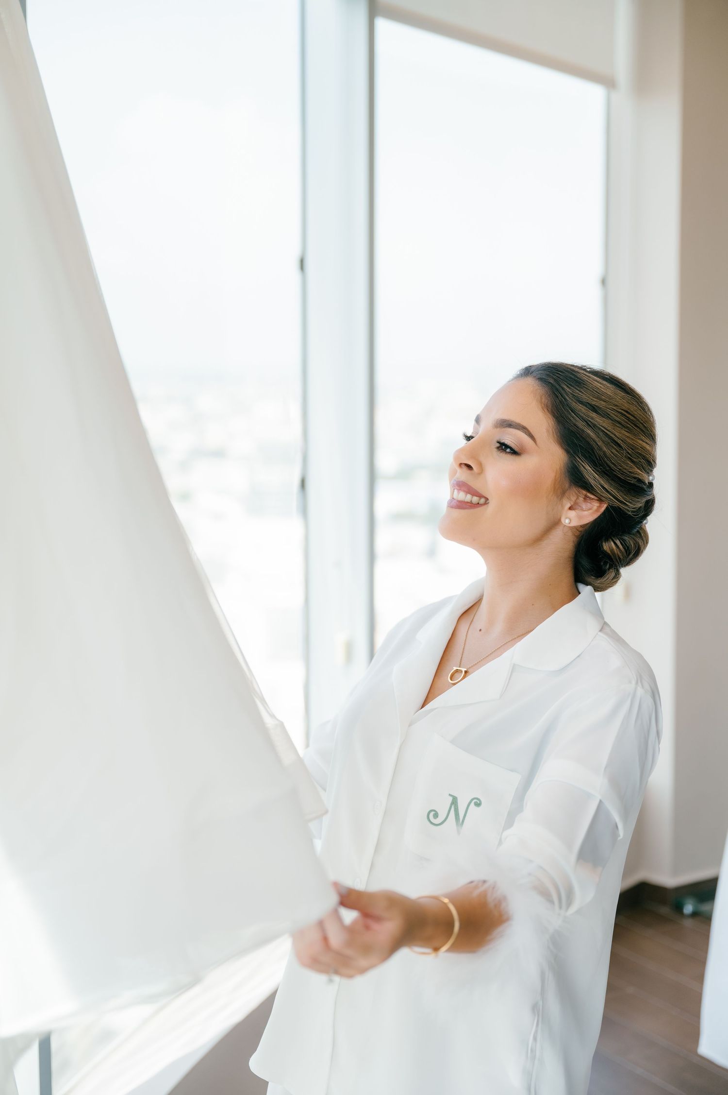 A joyful bride in a white robe dances among flowing white curtains in a bright sunlit room.