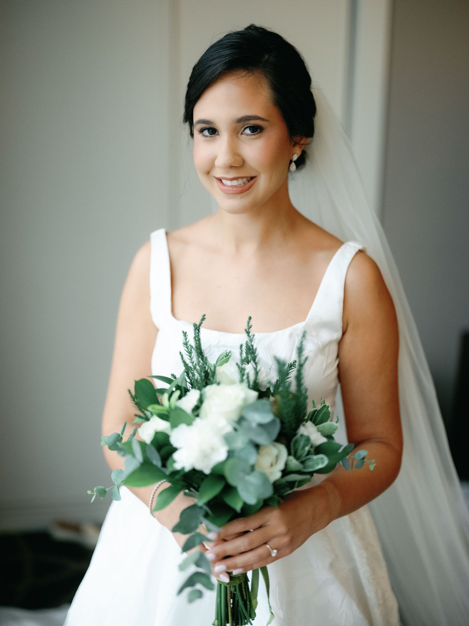 A bride in a classic white wedding dress holds a beautiful bouquet of white flowers and eucalyptus.