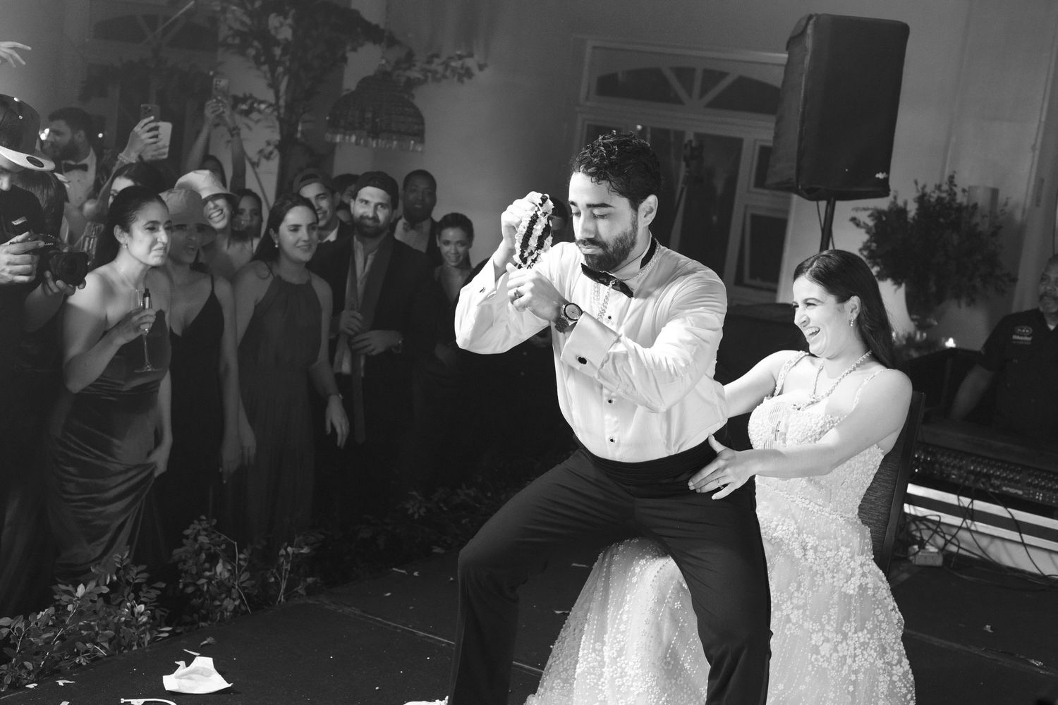 Black and white photo of wedding guests dancing and celebrating at a lively reception.
