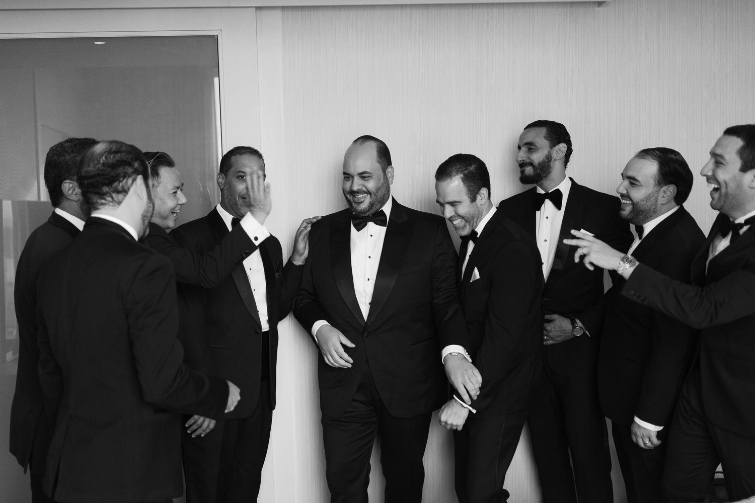 A black and white panoramic photo shows groomsmen in tuxedos gathered together at a formal event.