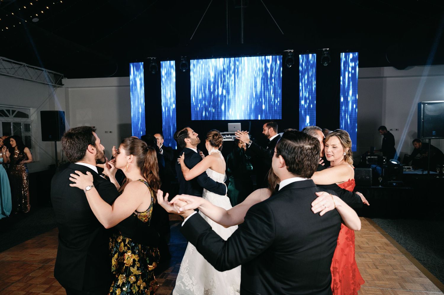 Wedding reception guests dancing and celebrating on a dark dance floor with blue lighting.